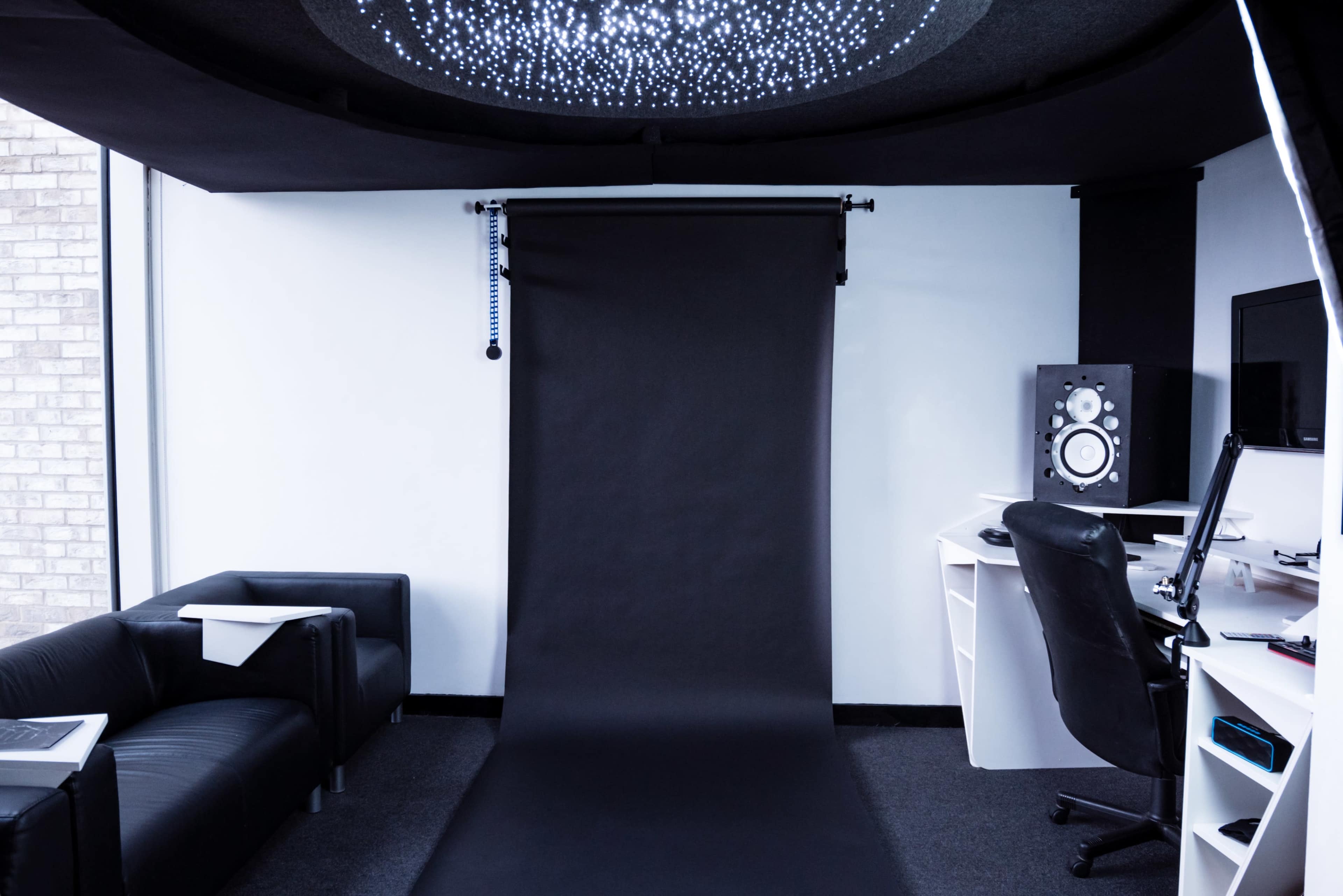 A photography studio with a black backdrop, a couch, a computer desk, and audio equipment.