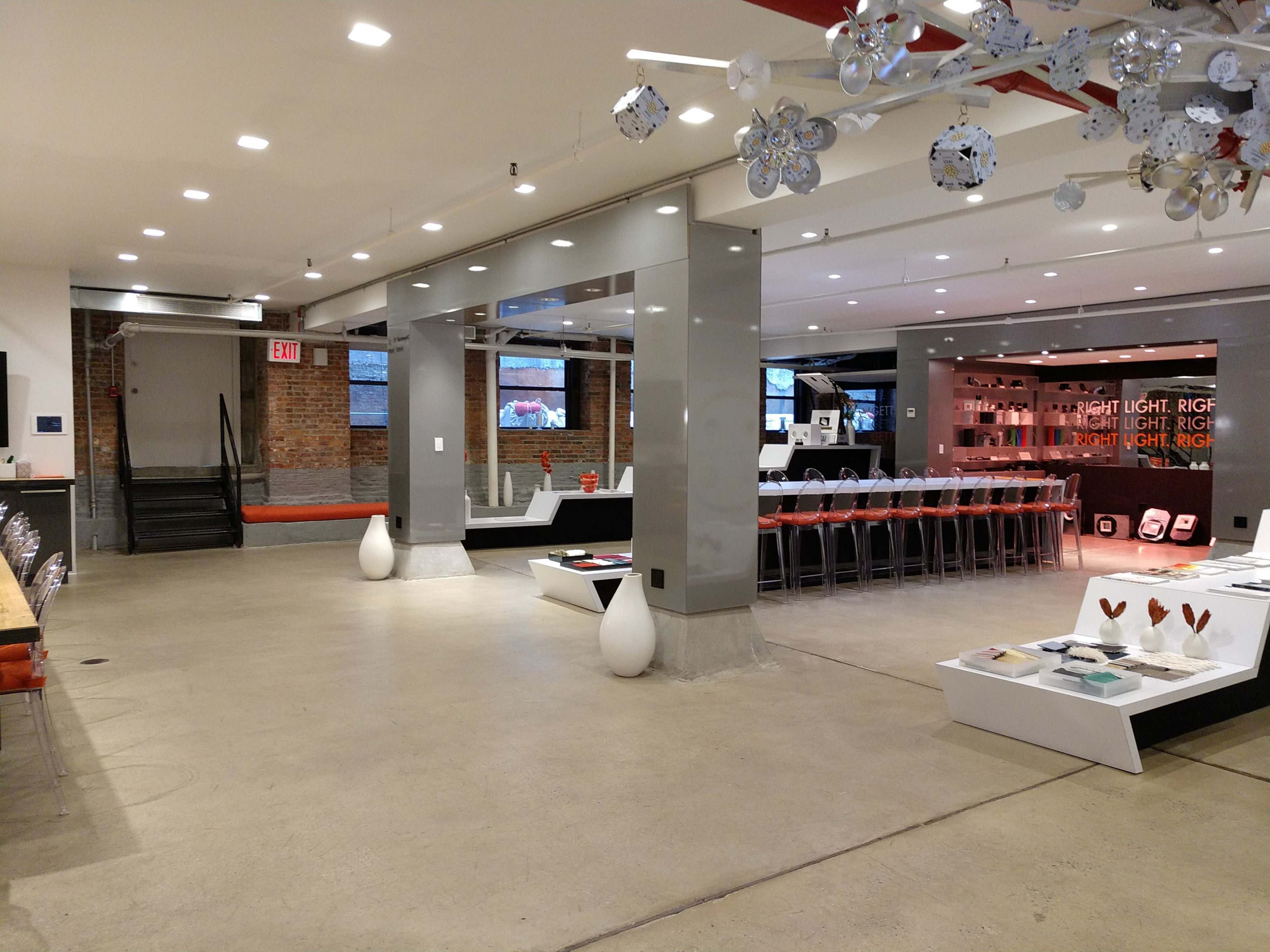 The image shows a modern, spacious interior of a retail space with a bar-style seating area, tables, and a sleek design featuring gray and white elements.