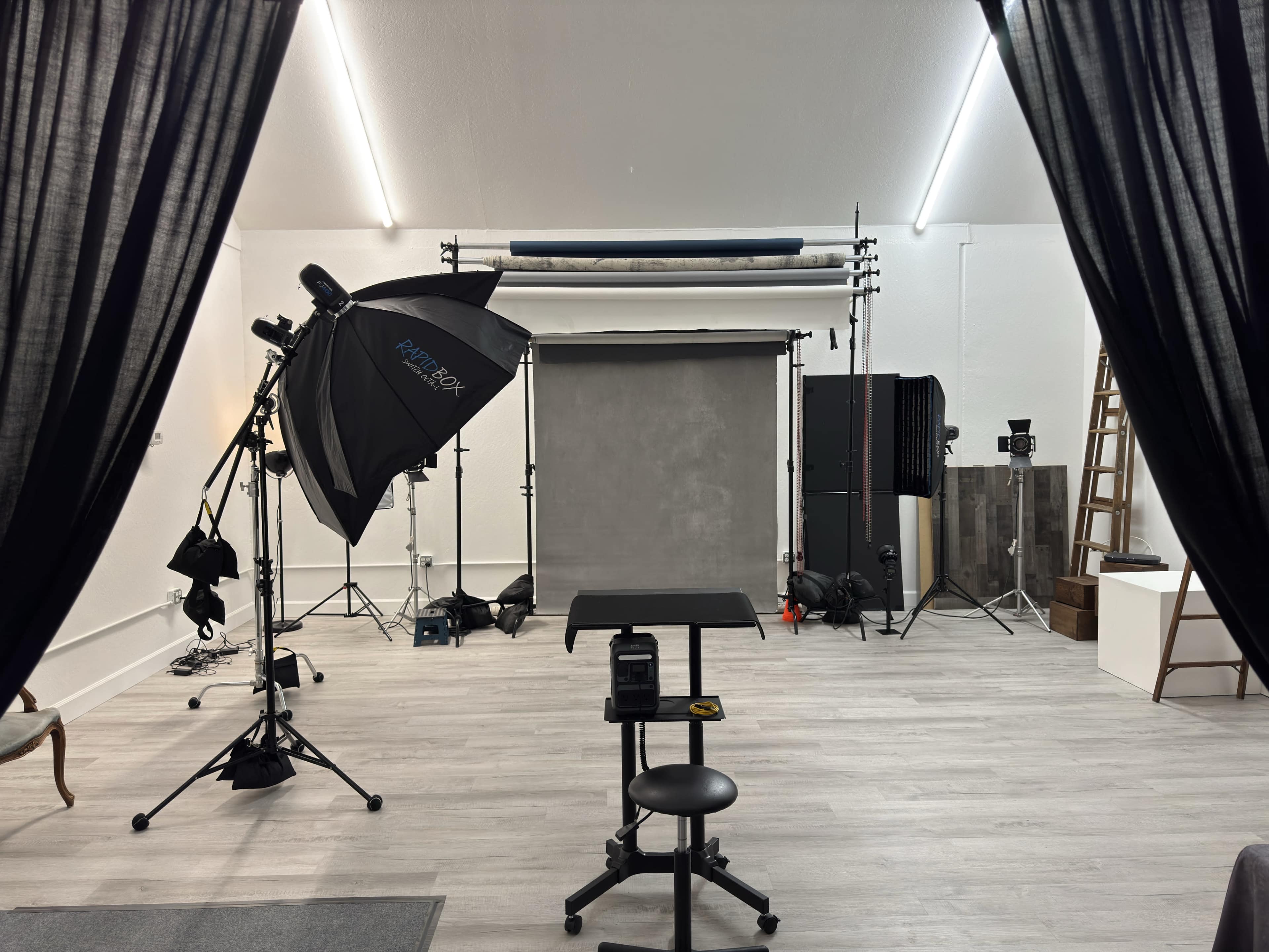 The image shows a photography studio featuring a backdrop, lighting equipment, a stool, and various props arranged for a photoshoot.