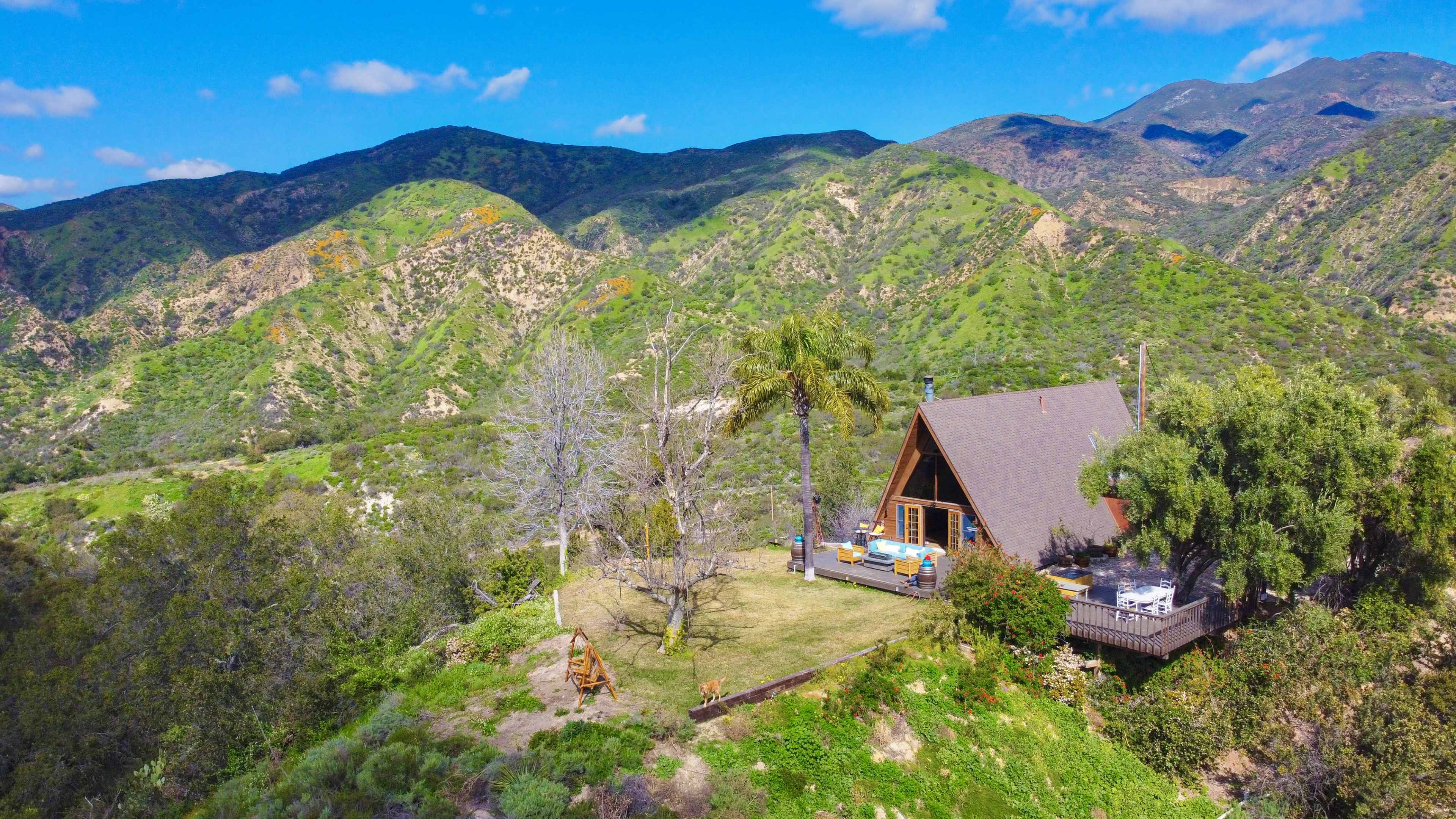 A cabin is situated on a grassy area surrounded by mountains and lush greenery.