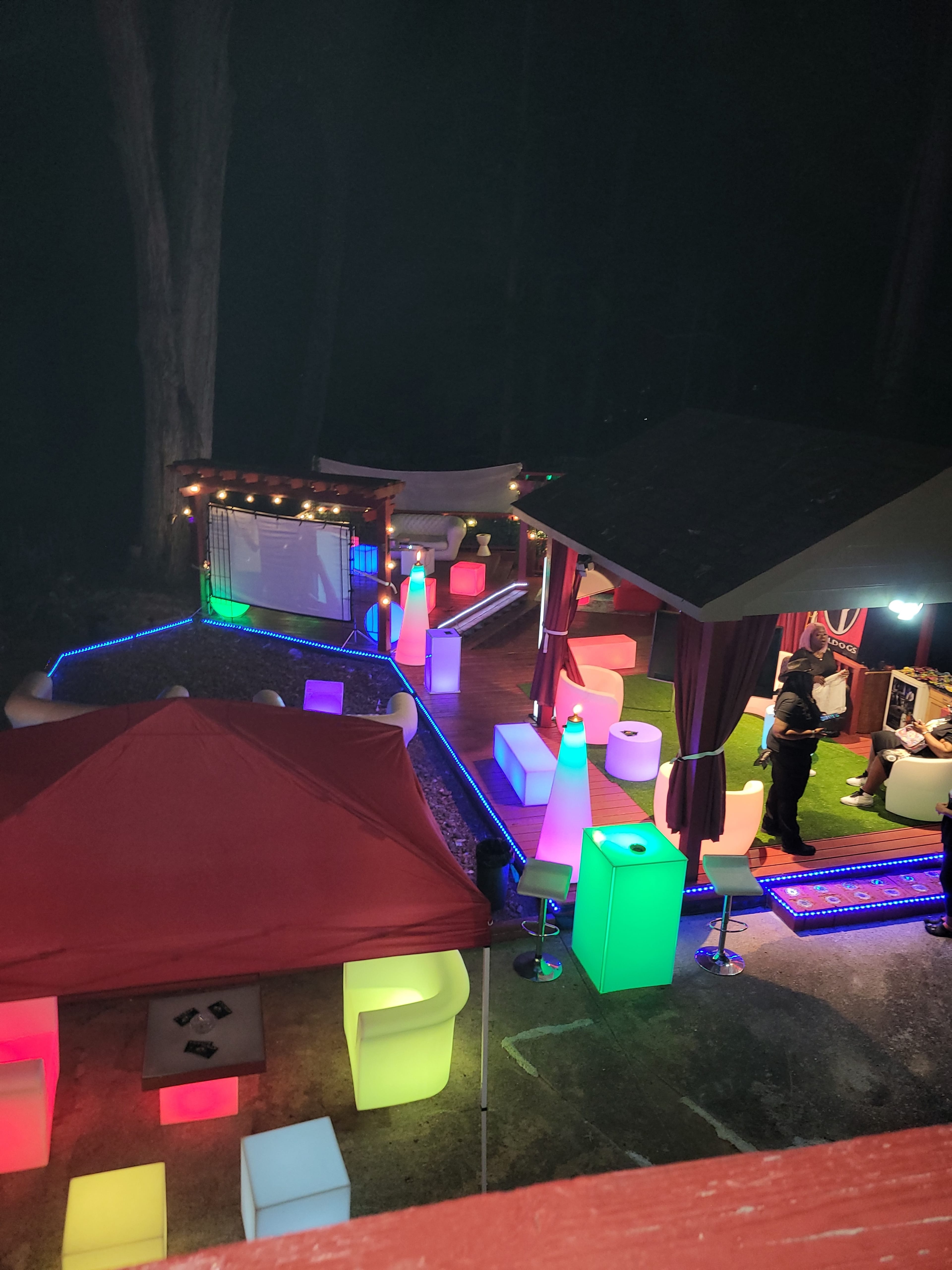 The image shows an outdoor party scene with illuminated furniture and tents set against a dark background.