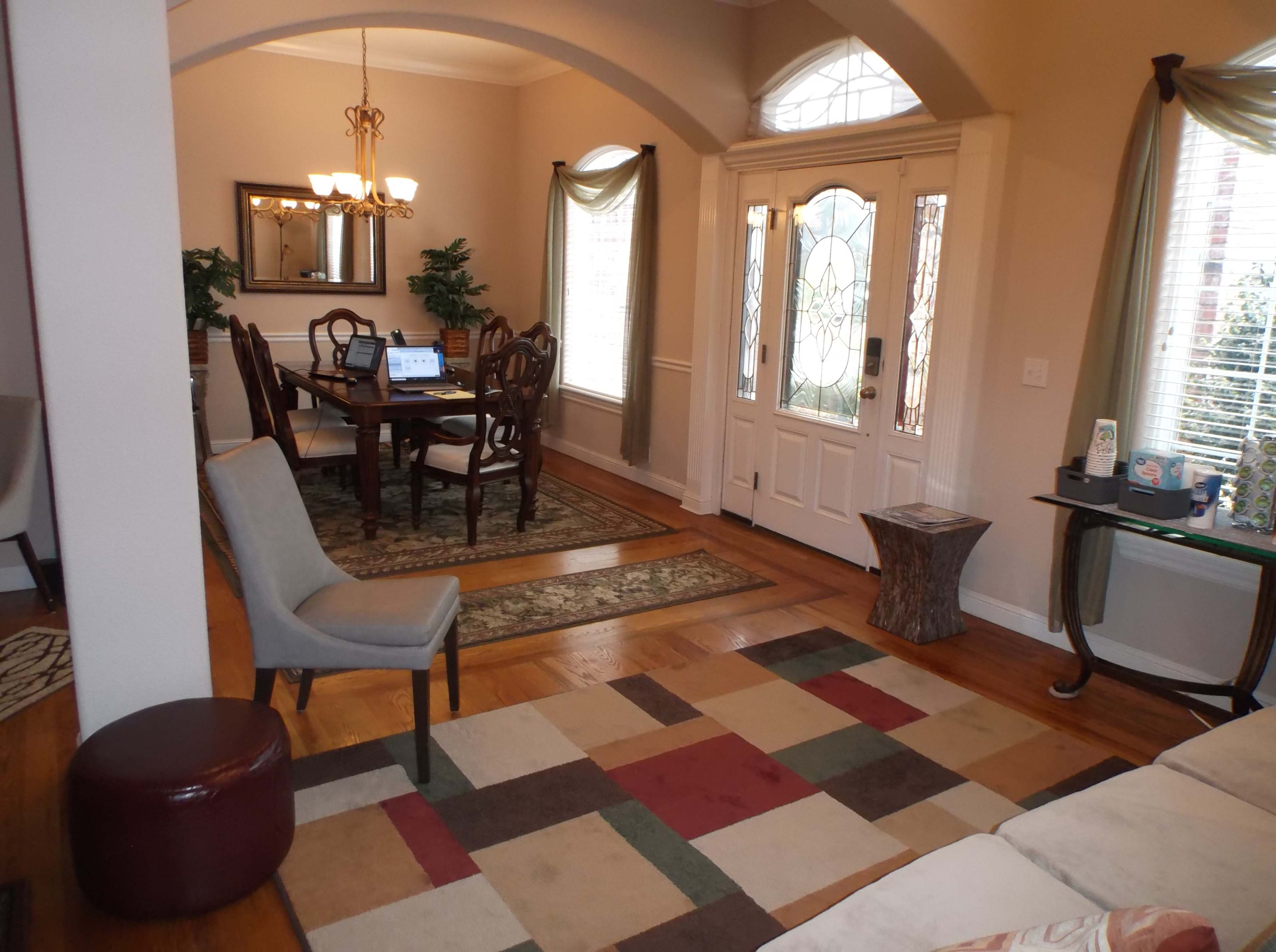 A spacious living area with hardwood floors, a dining table set for six, and a front entrance featuring large glass doors.