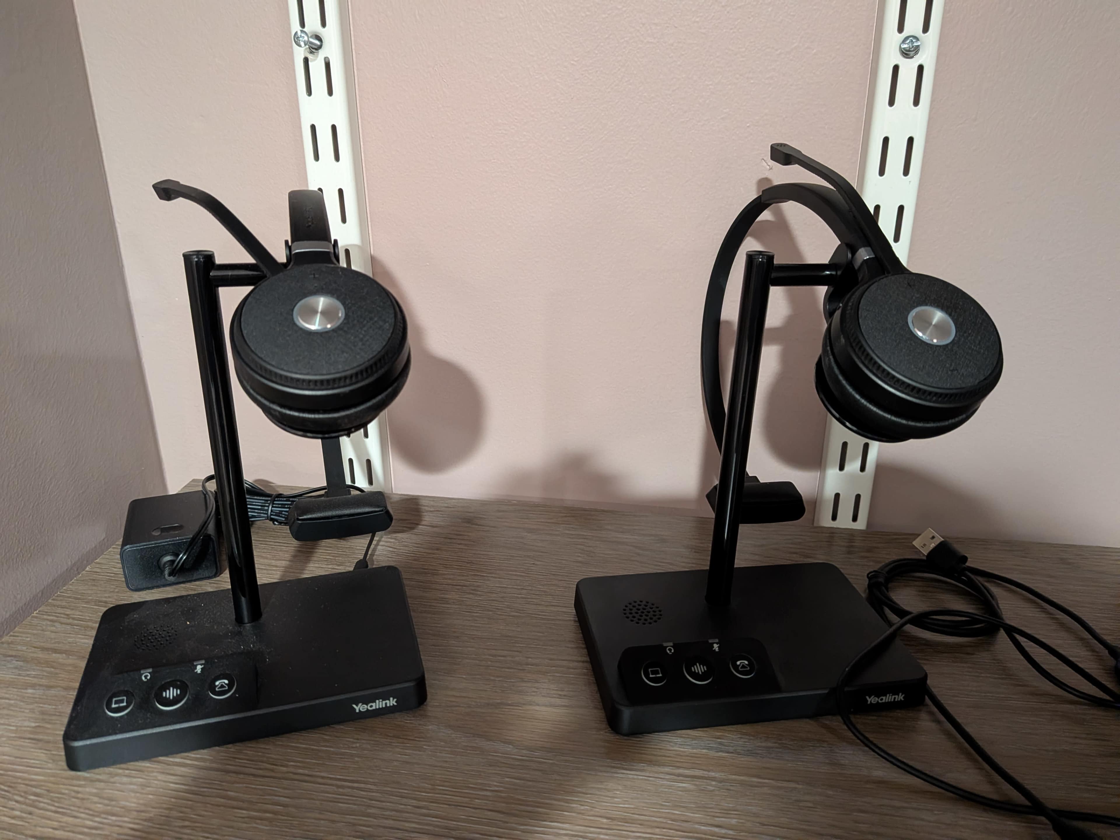 The image shows two black headsets mounted on stands on a wooden surface, with cables and control panels visible.