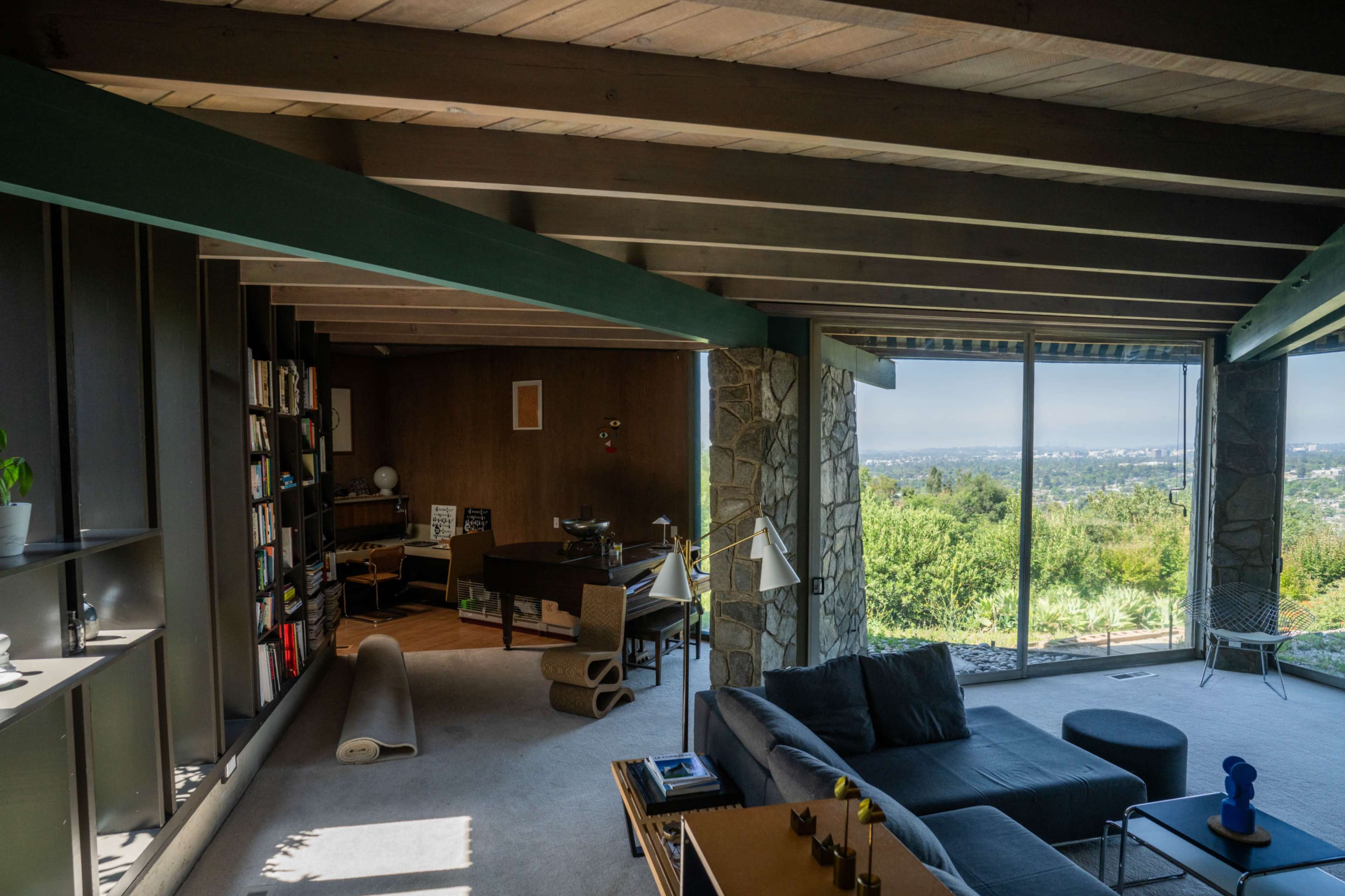 A spacious living room features large windows with a scenic view, stone and wooden accents, and modern furniture.