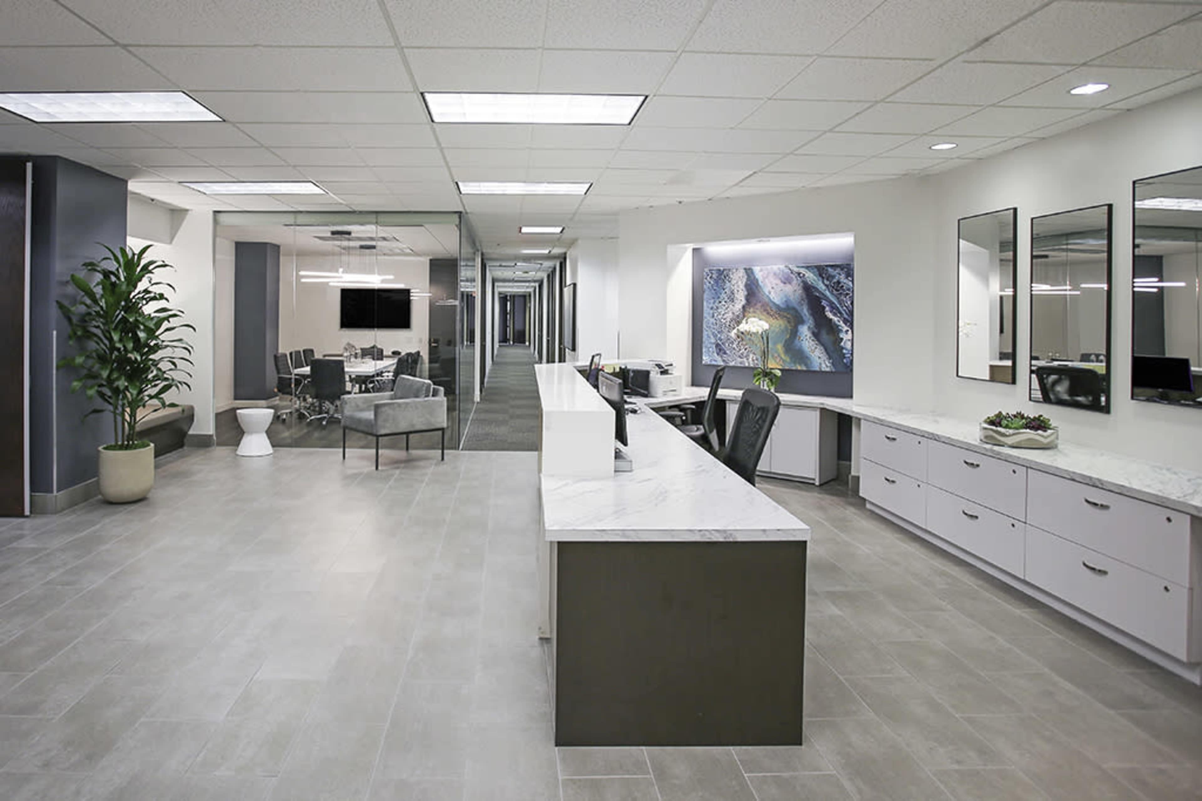 A modern office interior featuring a reception area with a marble countertop, sleek cabinets, and a hallway leading to conference rooms and workspaces.