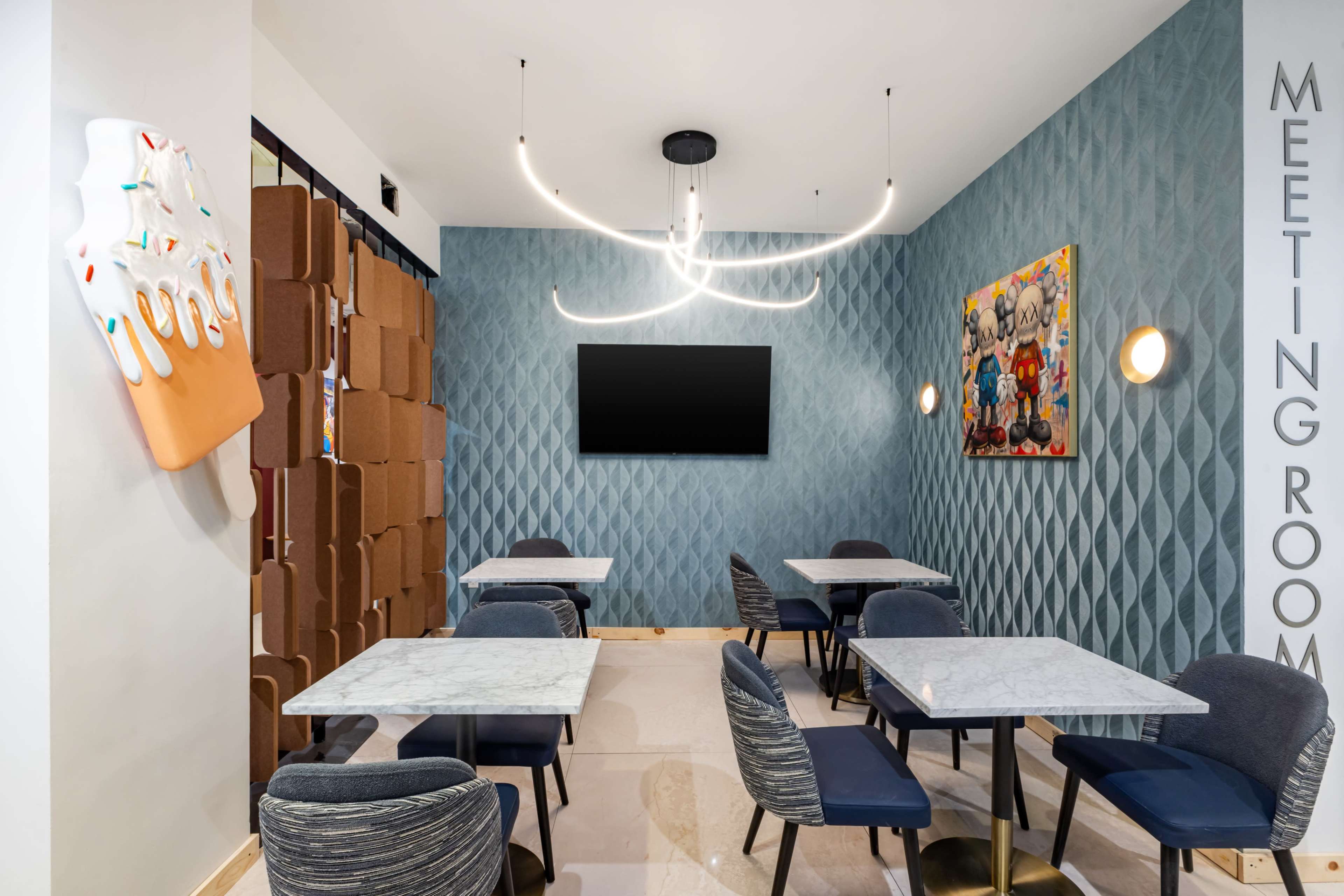 The image shows a modern meeting room with marble-topped tables, upholstered chairs, a decorative wall with artwork, and a unique light fixture.