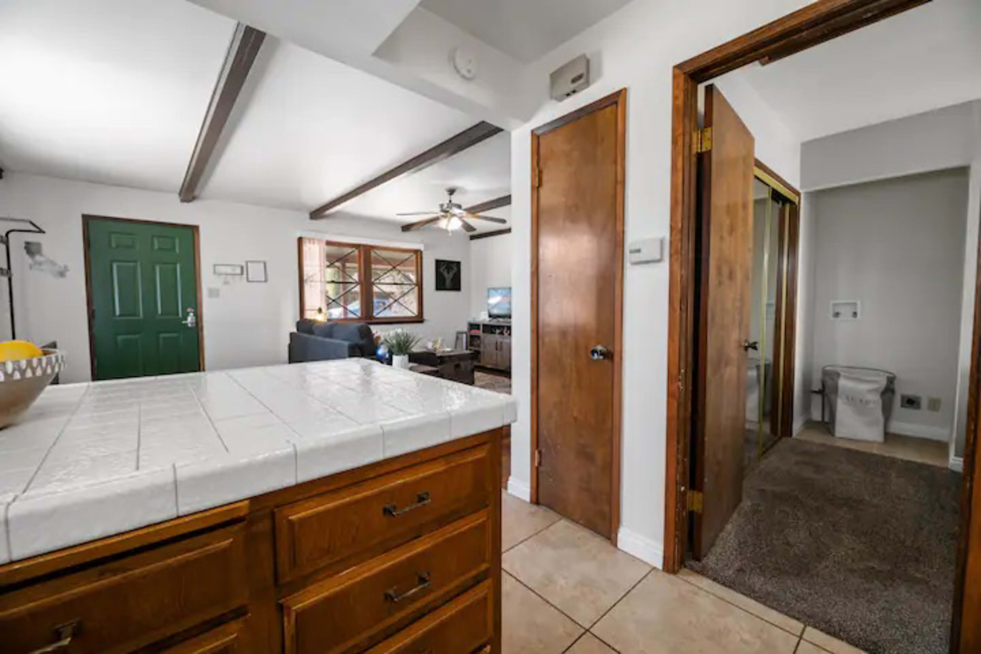 A view of a home's interior, featuring a kitchen with wooden cabinets, a doorway leading to a hallway, and an adjacent living area with a television.