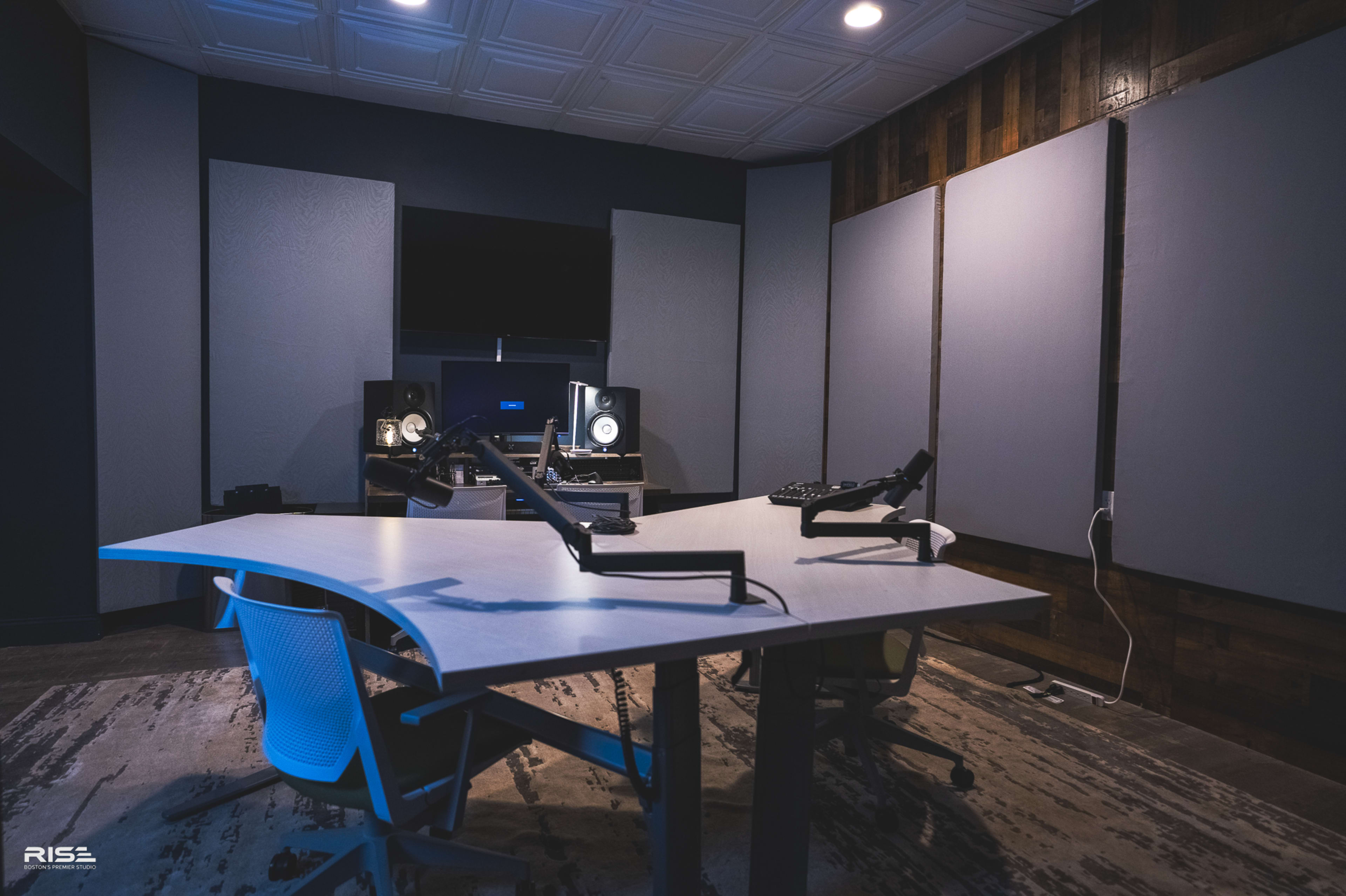 A modern audio recording studio features a large, curved table with two chairs, soundproof wall panels, and professional audio equipment.
