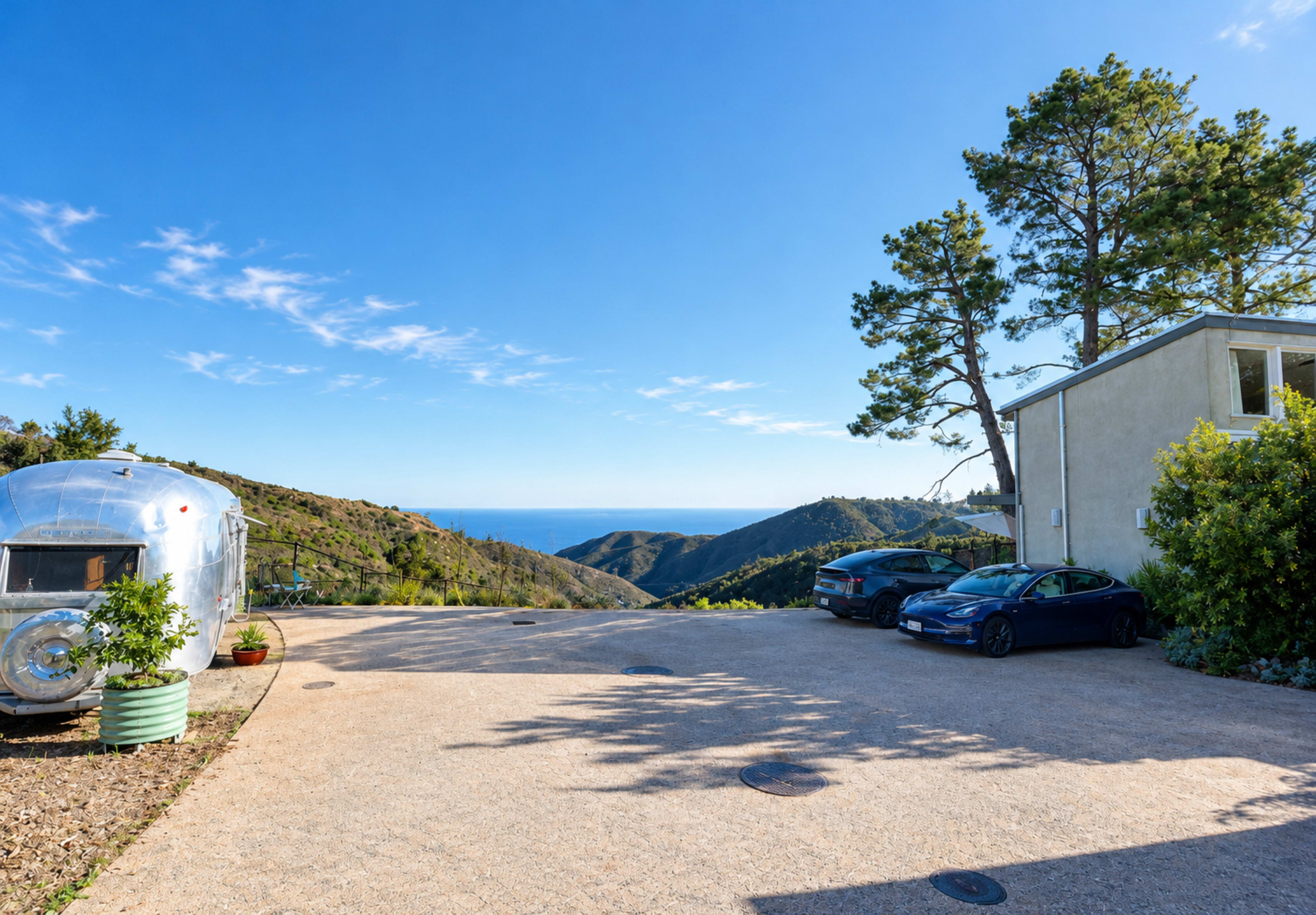 The image features a scenic view of a coastal landscape with rolling hills, an Airstream trailer parked on a gravel driveway, and a modern building, all under a clear blue sky.