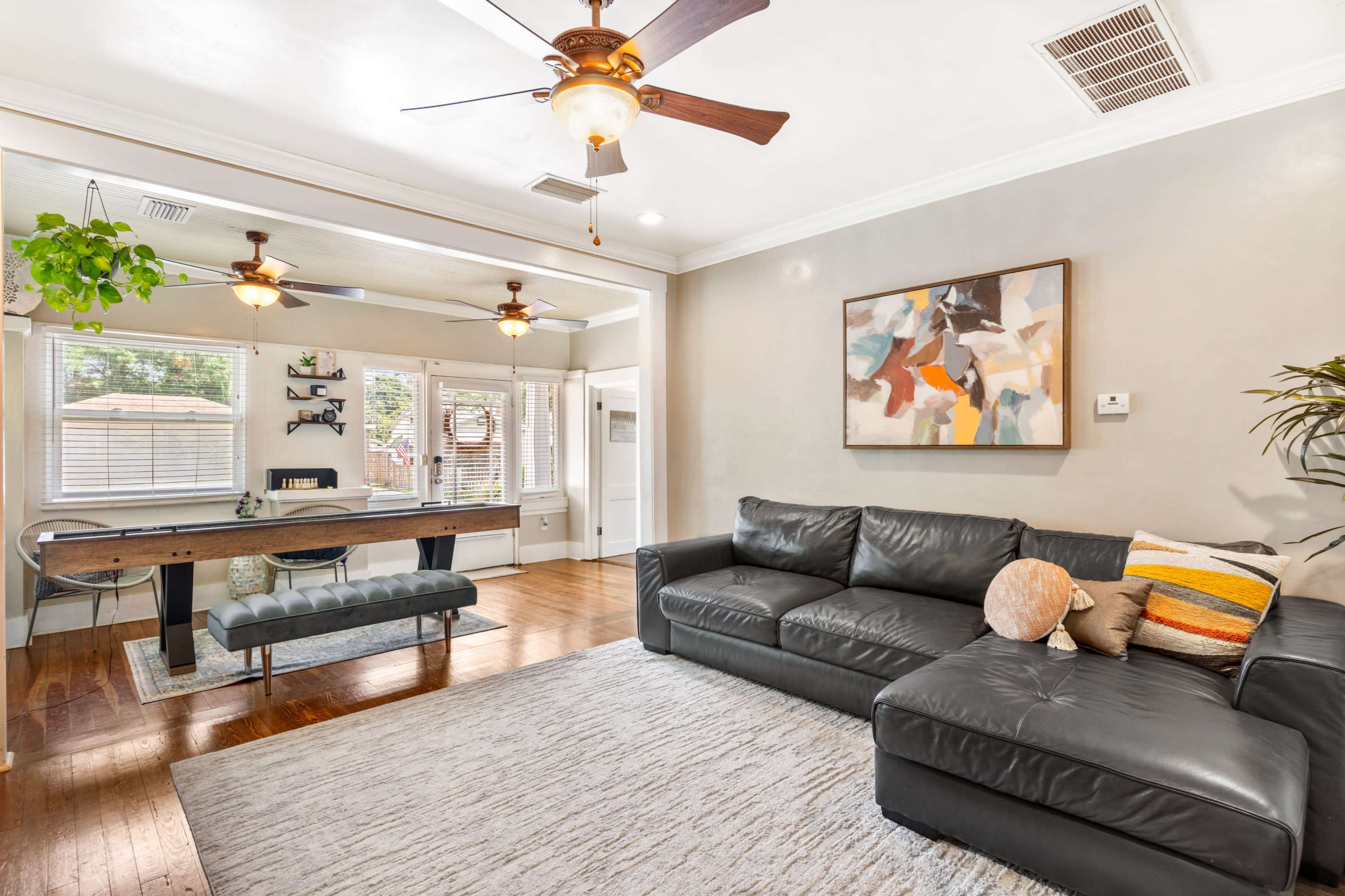 A living room with a black leather sectional sofa, a coffee table, a desk area with a window, and two ceiling fans.