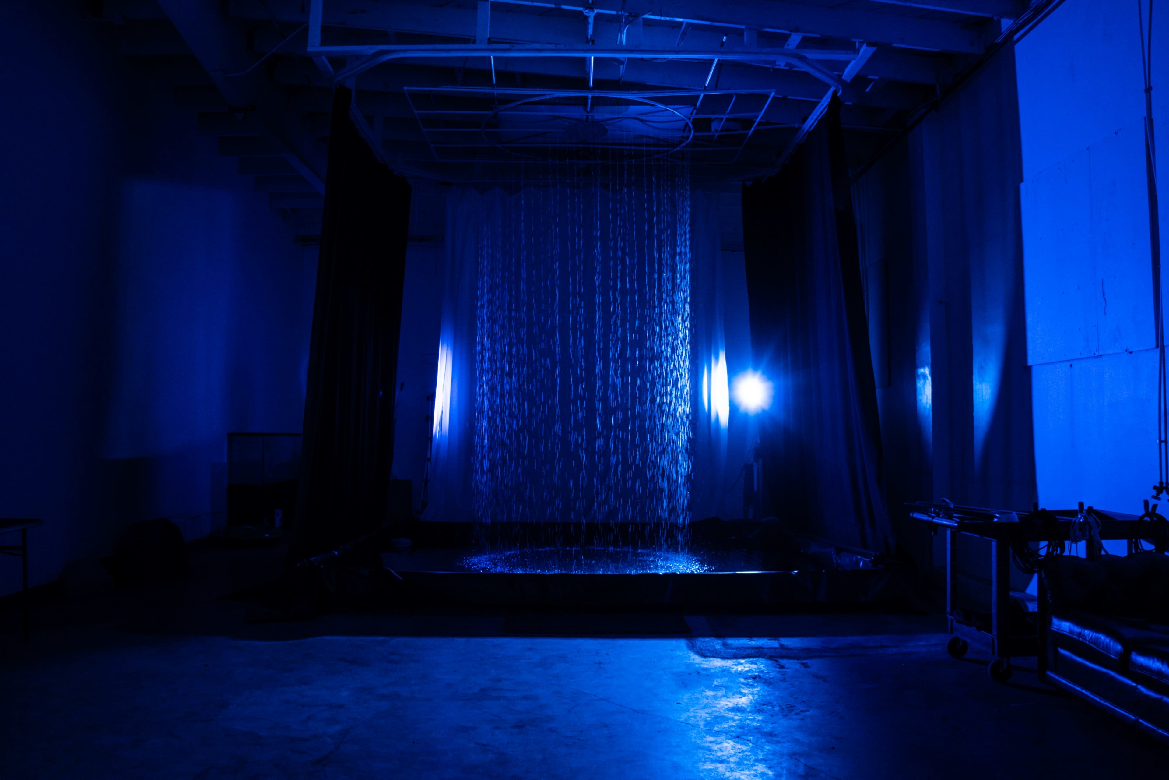 A waterfall cascades down in a dimly lit room with blue lighting, creating a reflective surface on the floor.
