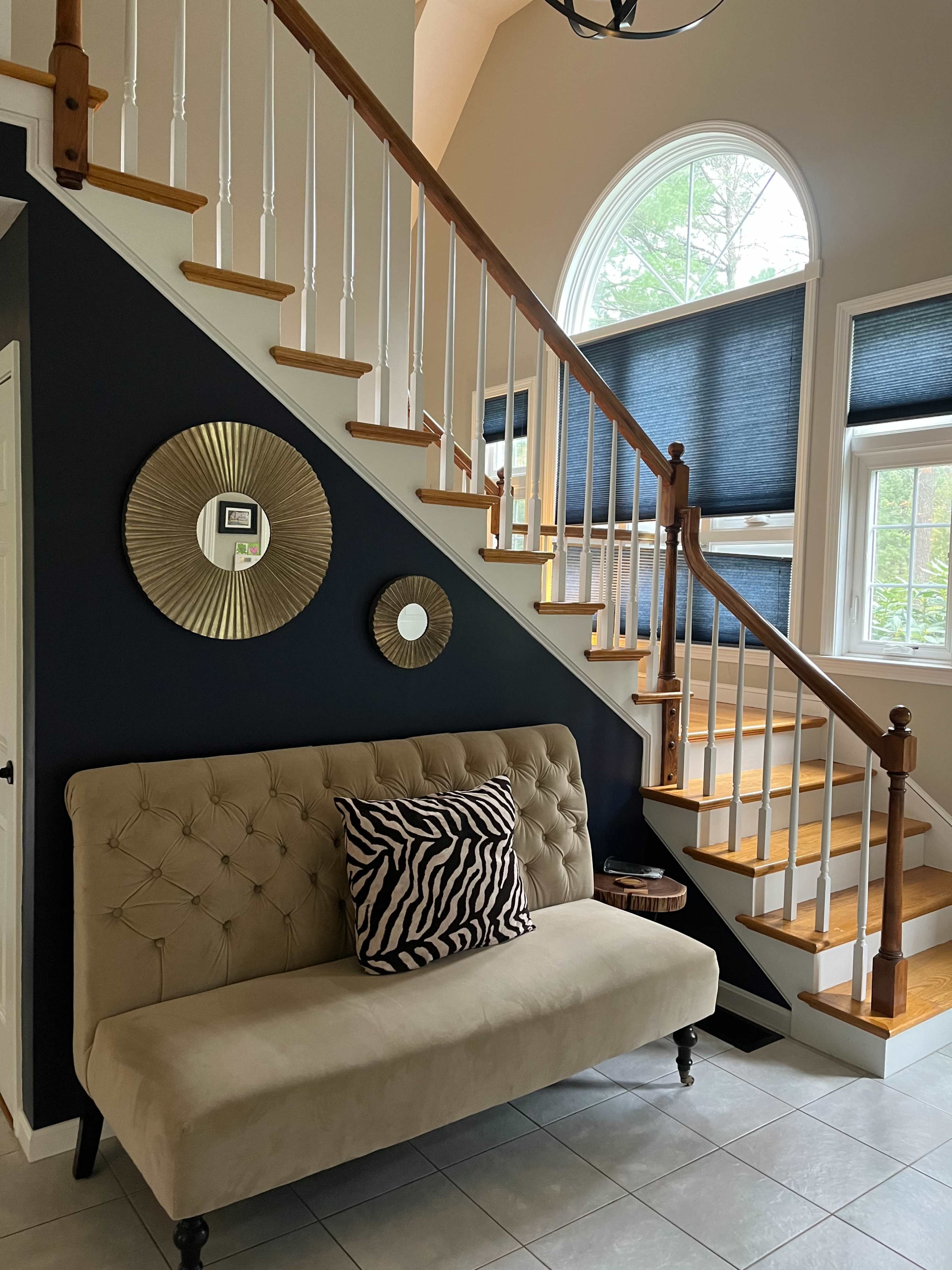 A staircase with wooden steps and a decorative landing, along with a beige tufted bench and circular mirrors on a dark wall.