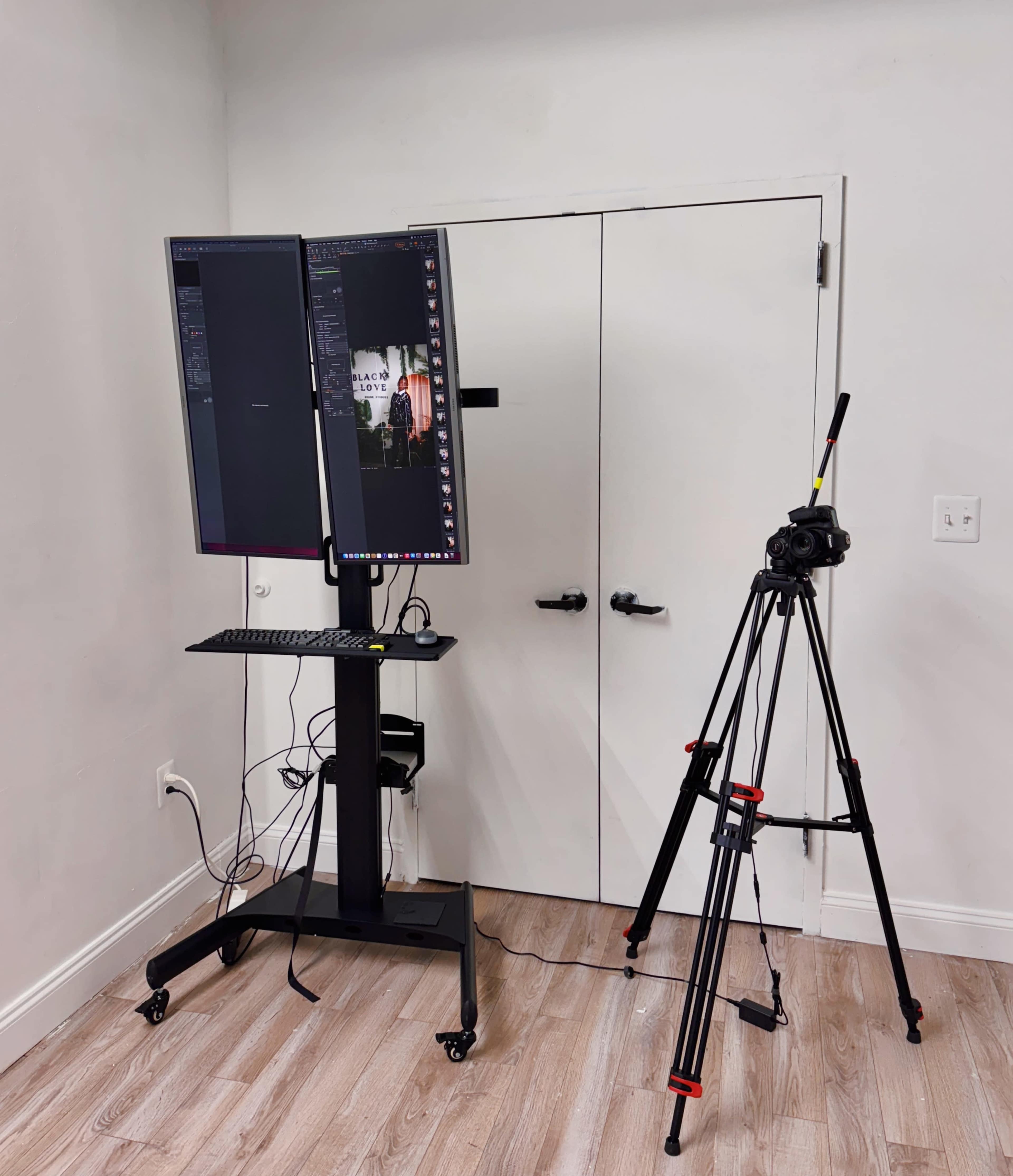 The image shows a workstation with two mounted monitors, a keyboard, and a camera on a tripod facing a closed white door.