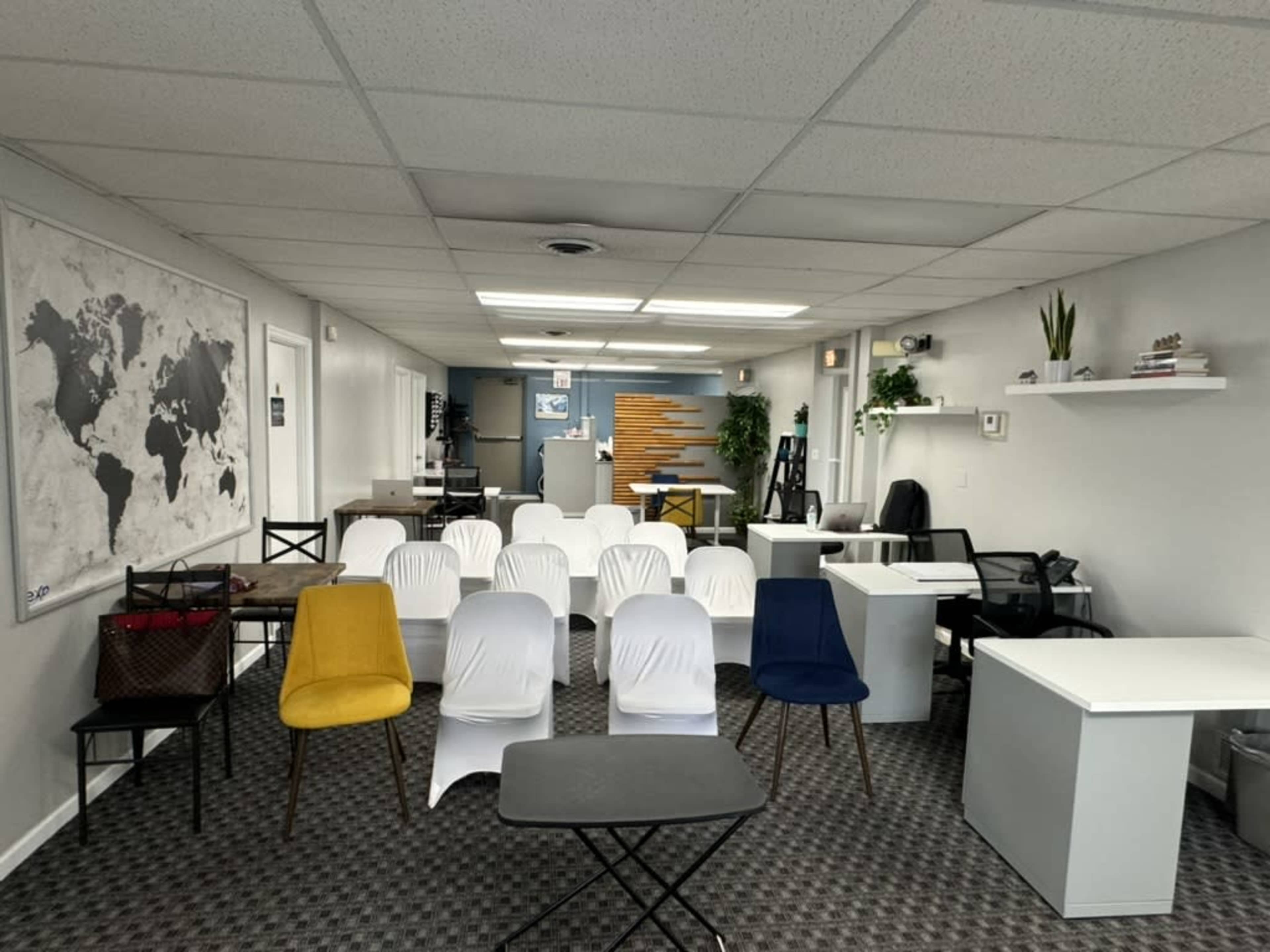 A spacious office setting with several chairs arranged in rows facing a desk area, surrounded by tables and wall decorations, including a world map.