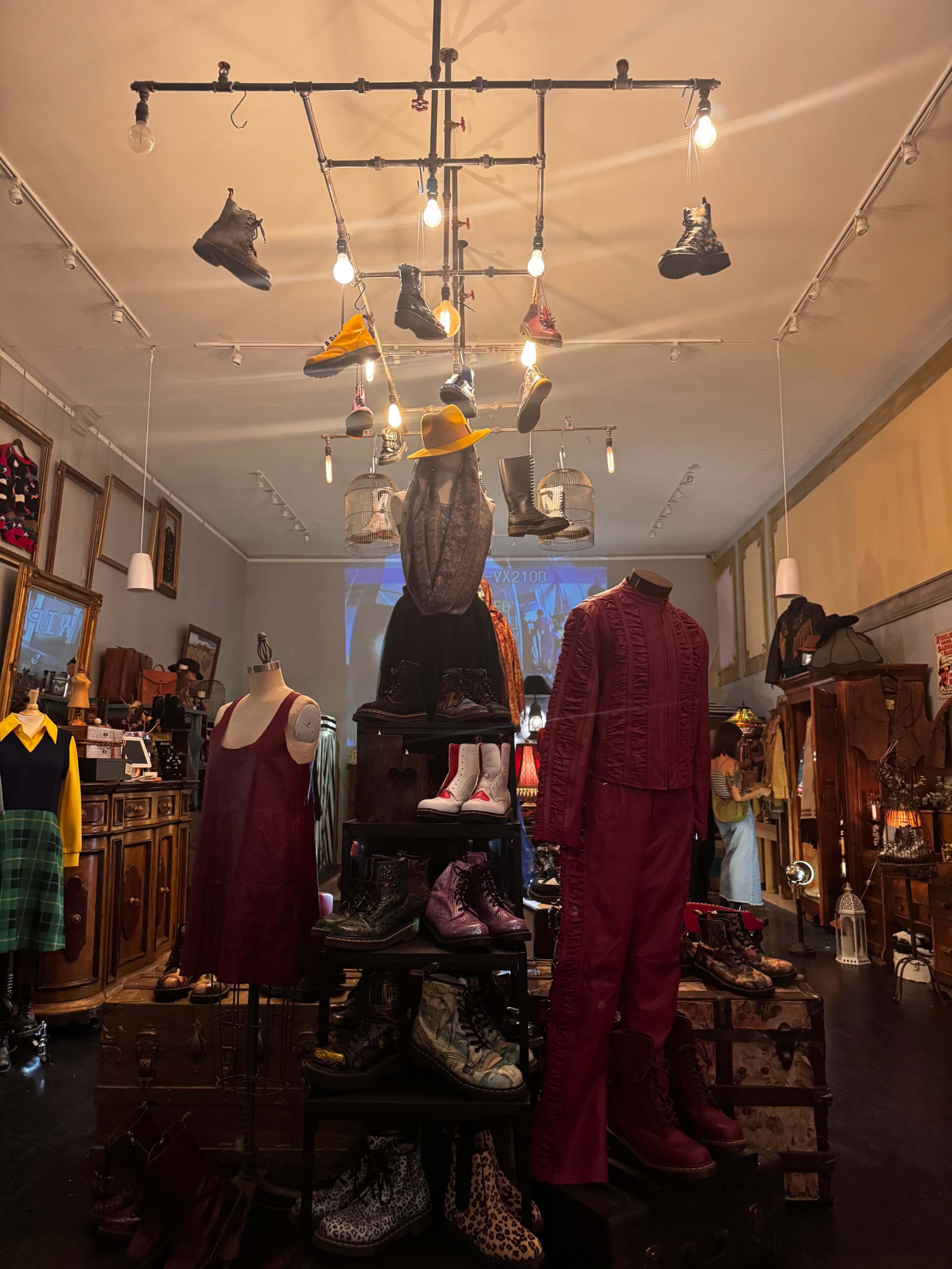The image depicts a vintage clothing store with a display of various shoes and garments arranged on a tiered display, illuminated by overhead lights.