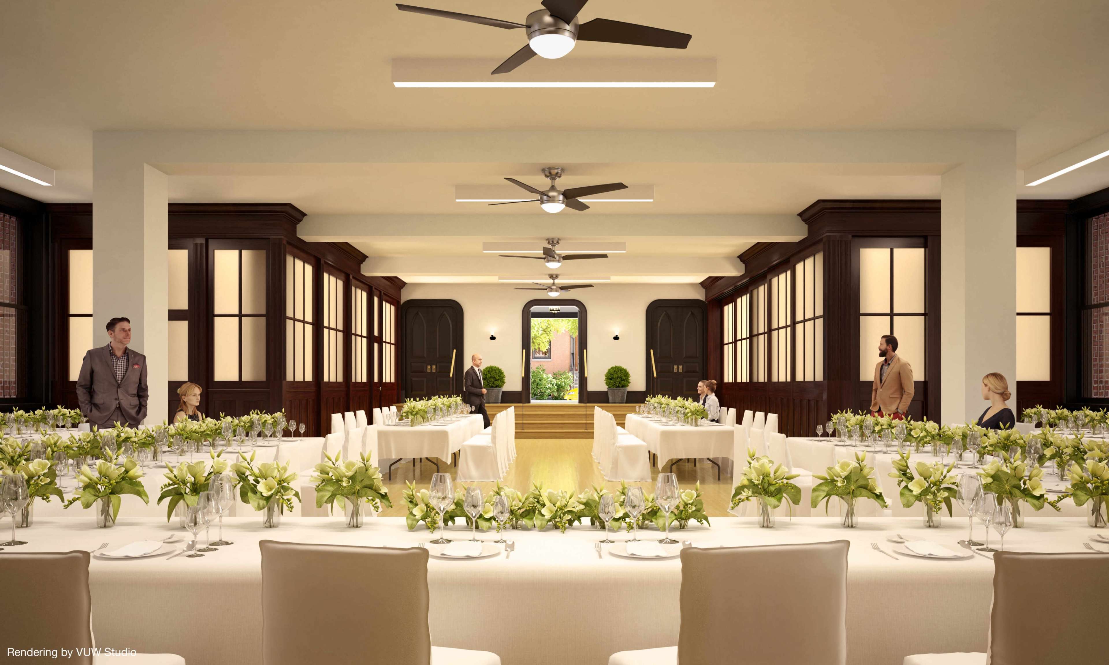 An elegantly arranged banquet room with long tables adorned with floral centerpieces and several people standing and sitting throughout the space.