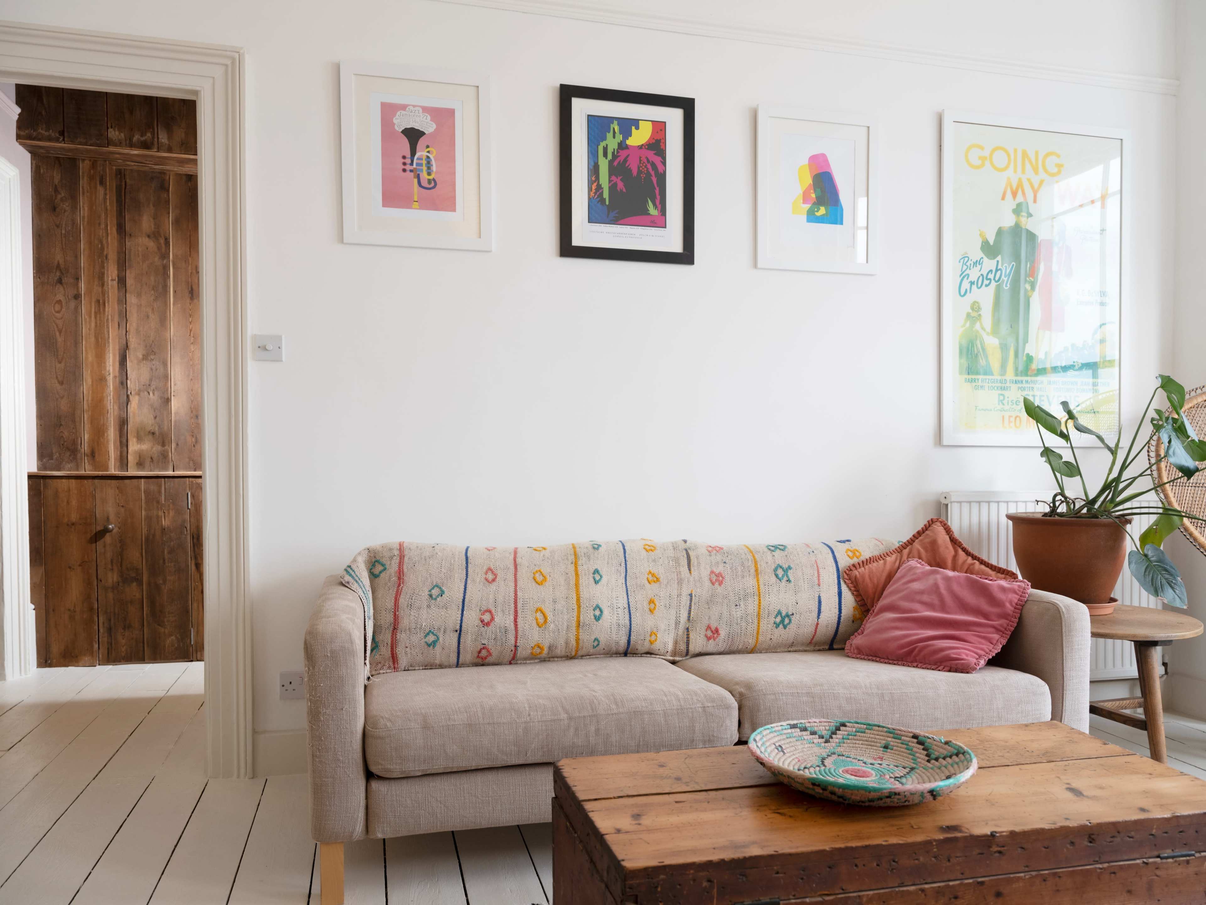 A living room with a beige couch adorned with a colorful patterned throw, a wooden coffee table, and framed artwork on the wall.