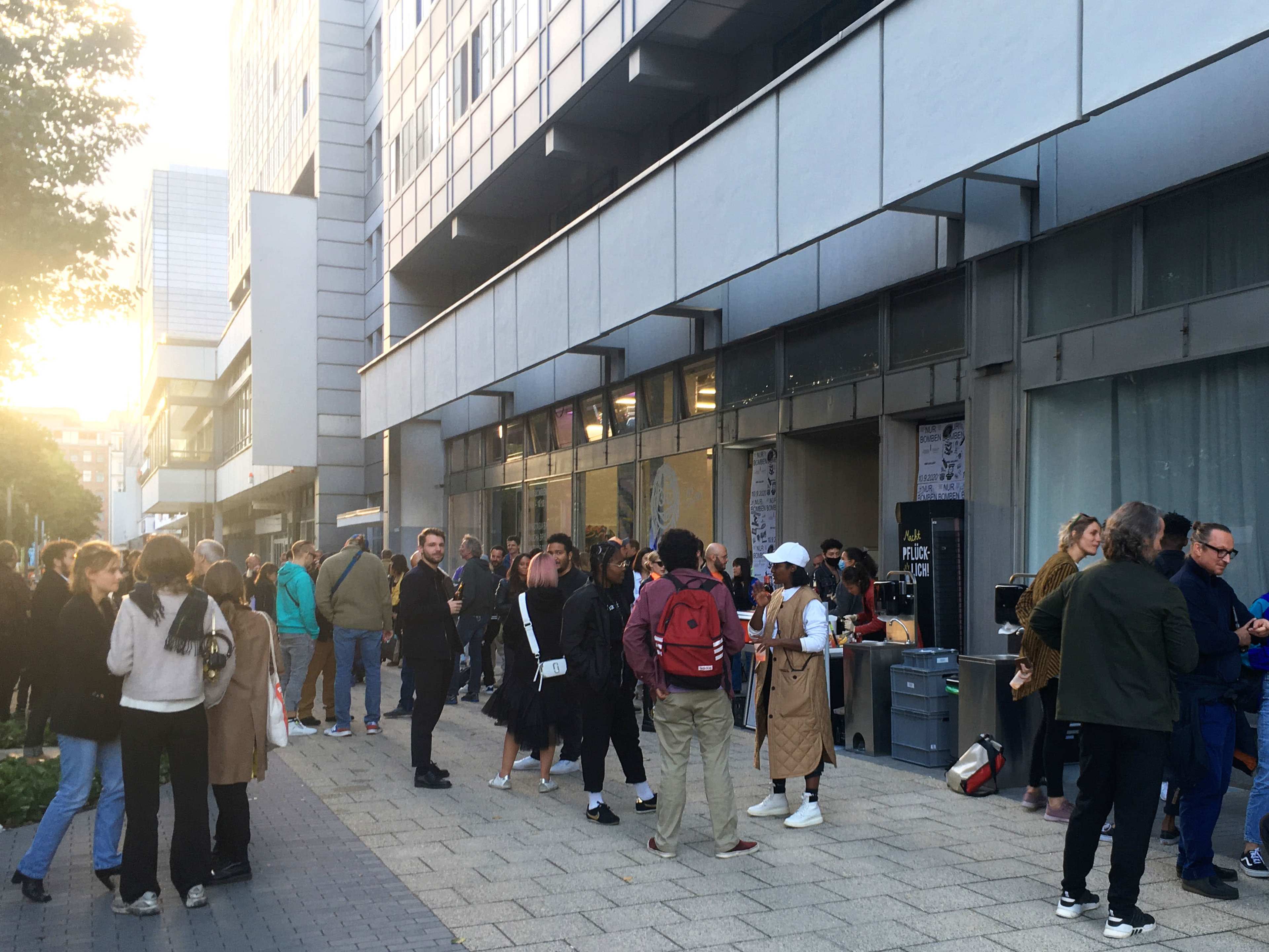 A crowd of people gathers in front of a building, with some individuals interacting and others waiting in line.
