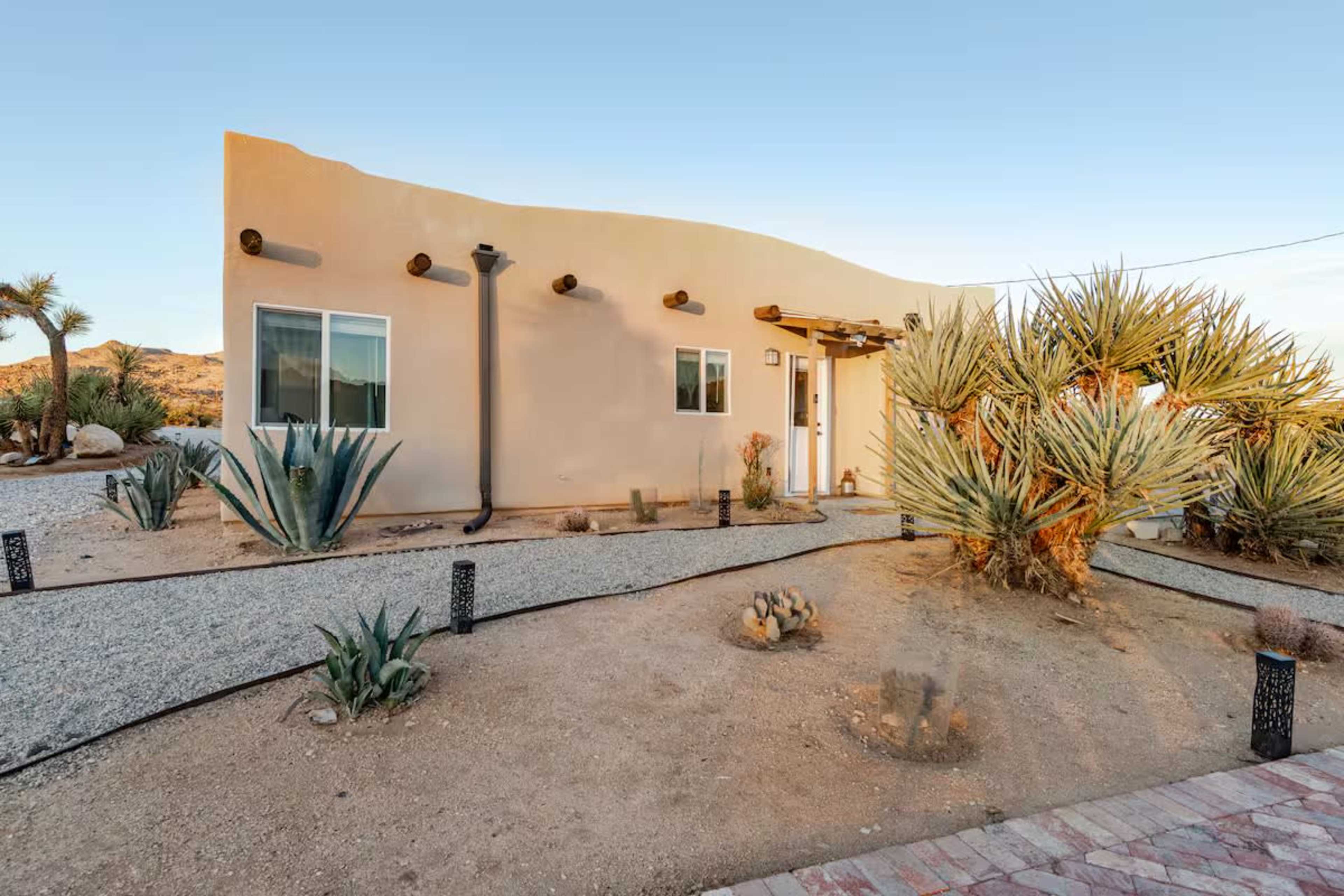 The image shows a single-story, adobe-style house surrounded by desert landscaping and succulents.
