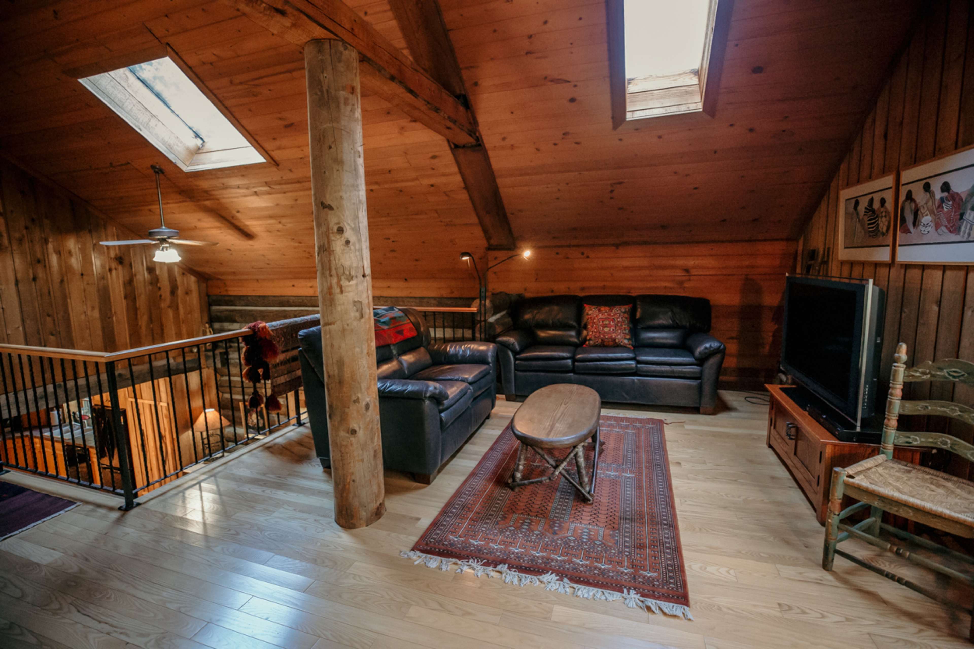 A wooden loft with a leather sectional sofa, a coffee table, and skylights illuminating the space.