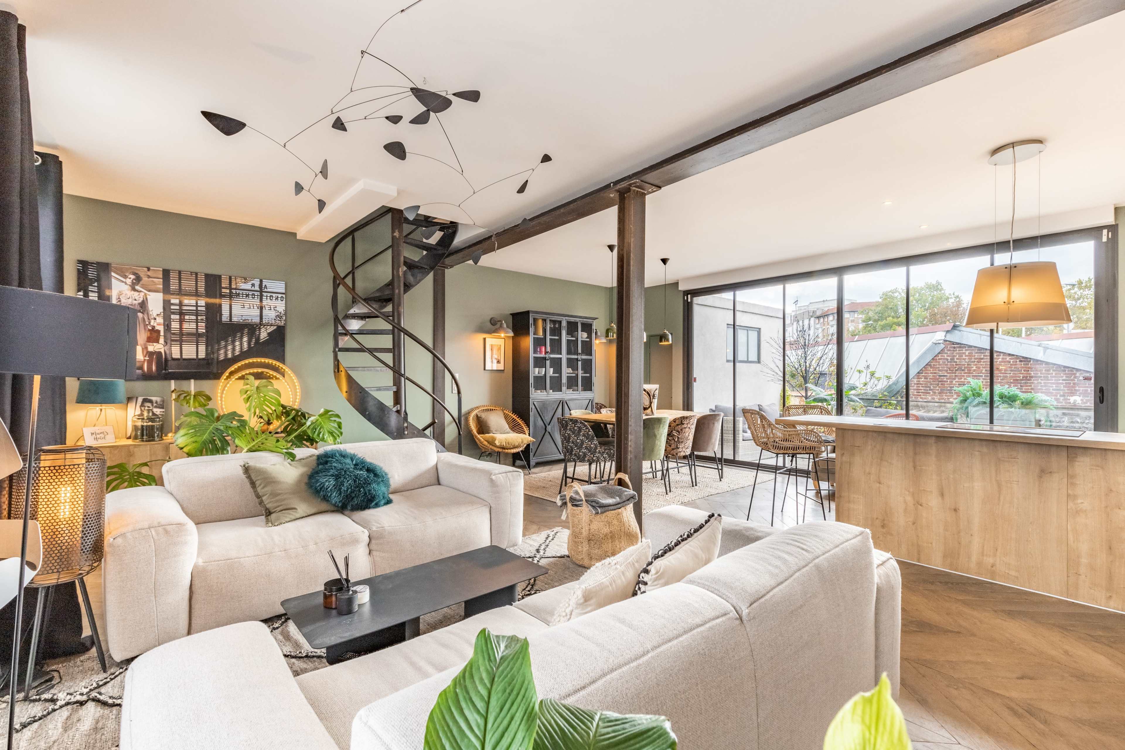 A modern living space featuring a spiral staircase, two sofas, a dining area, and large windows overlooking an outdoor view.