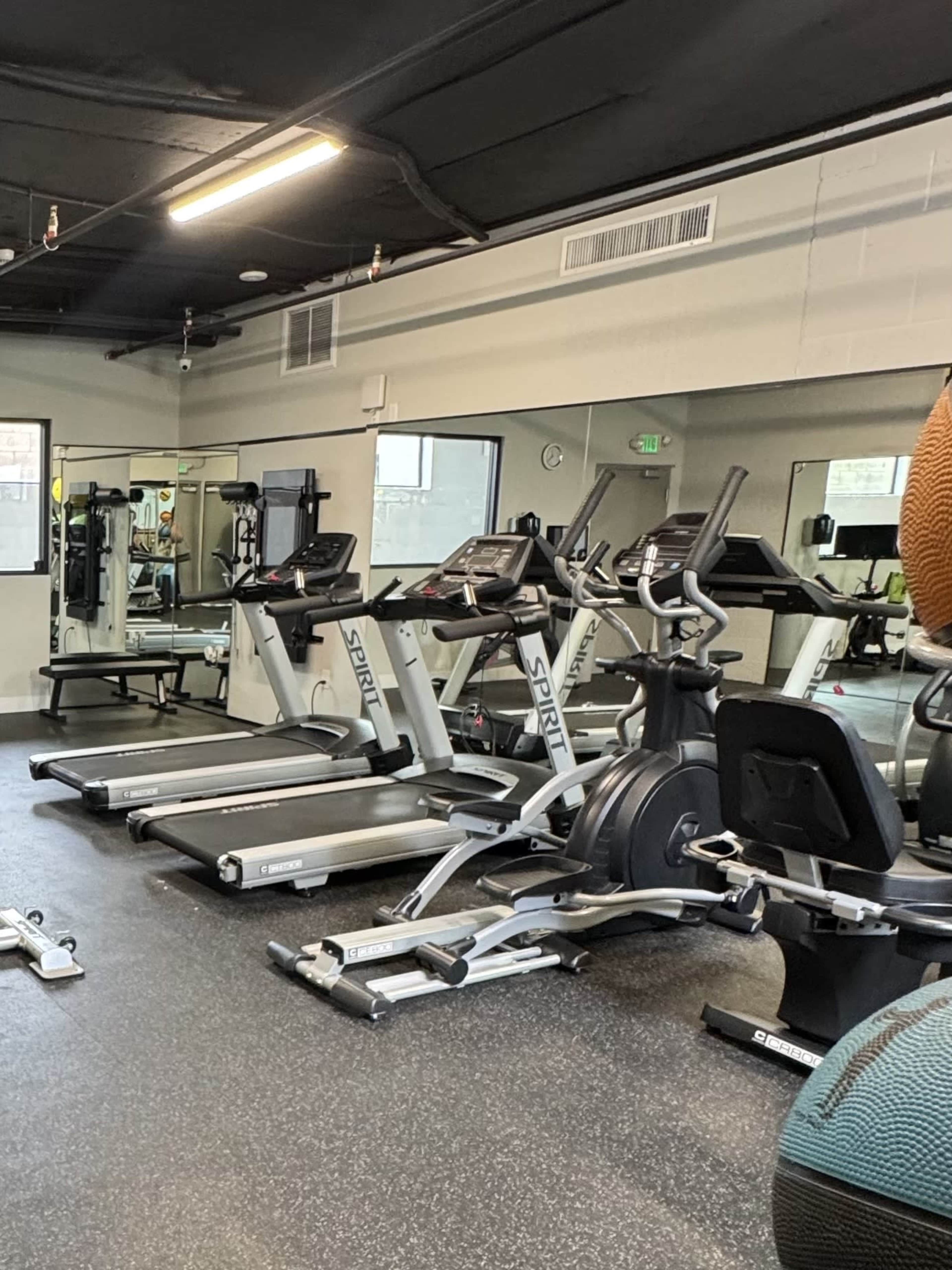 The image shows a fitness gym with various exercise machines, including treadmills and ellipticals, arranged in a well-lit space.