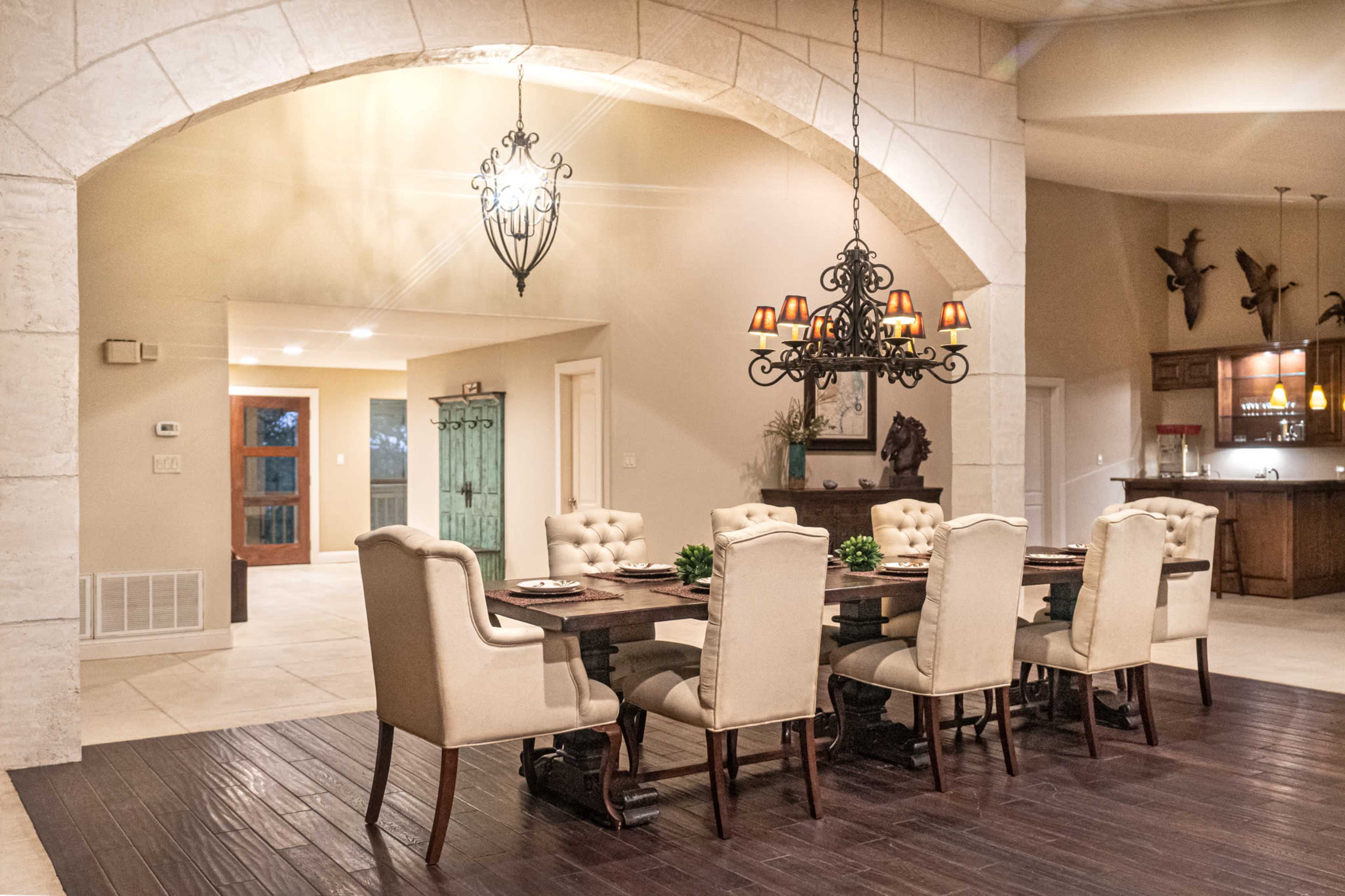 A spacious dining area features a long wooden table surrounded by upholstered chairs under a decorative chandelier.