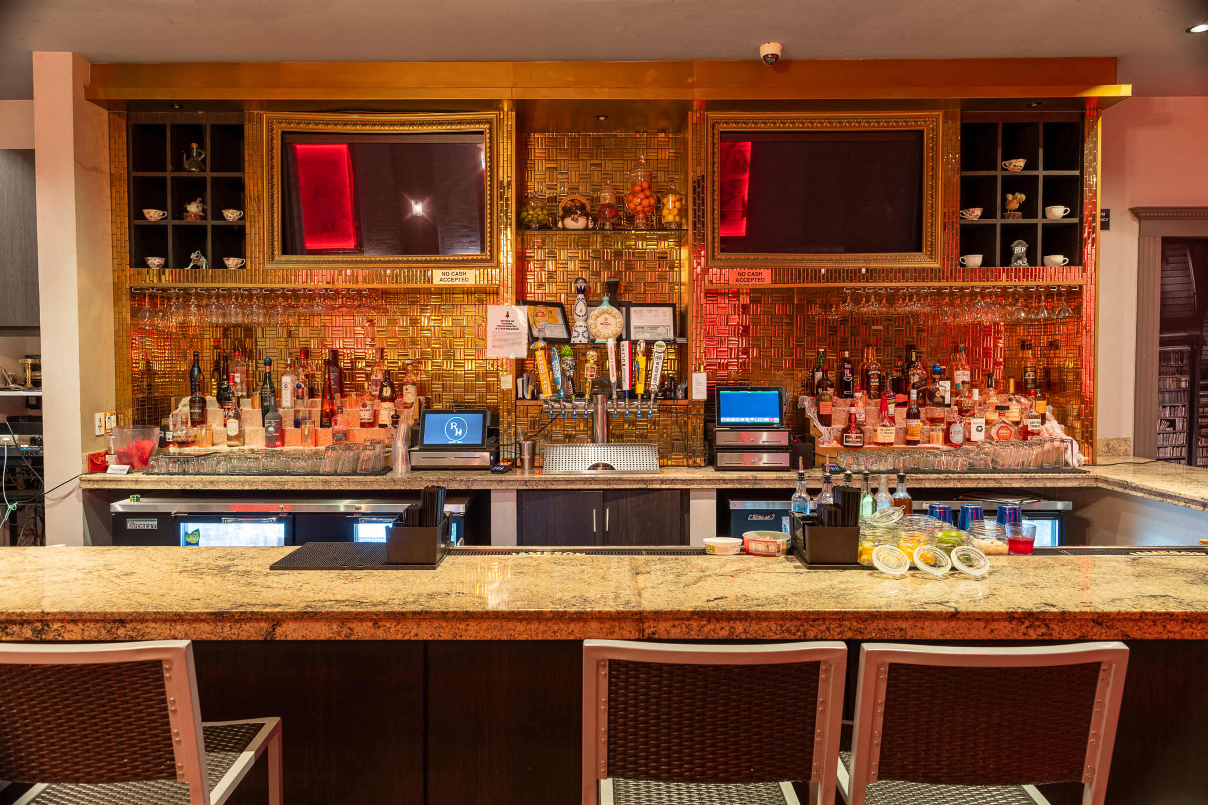 A well-stocked bar with a granite countertop, featuring various bottles of alcohol, two screens, and a selection of drinks displayed prominently.