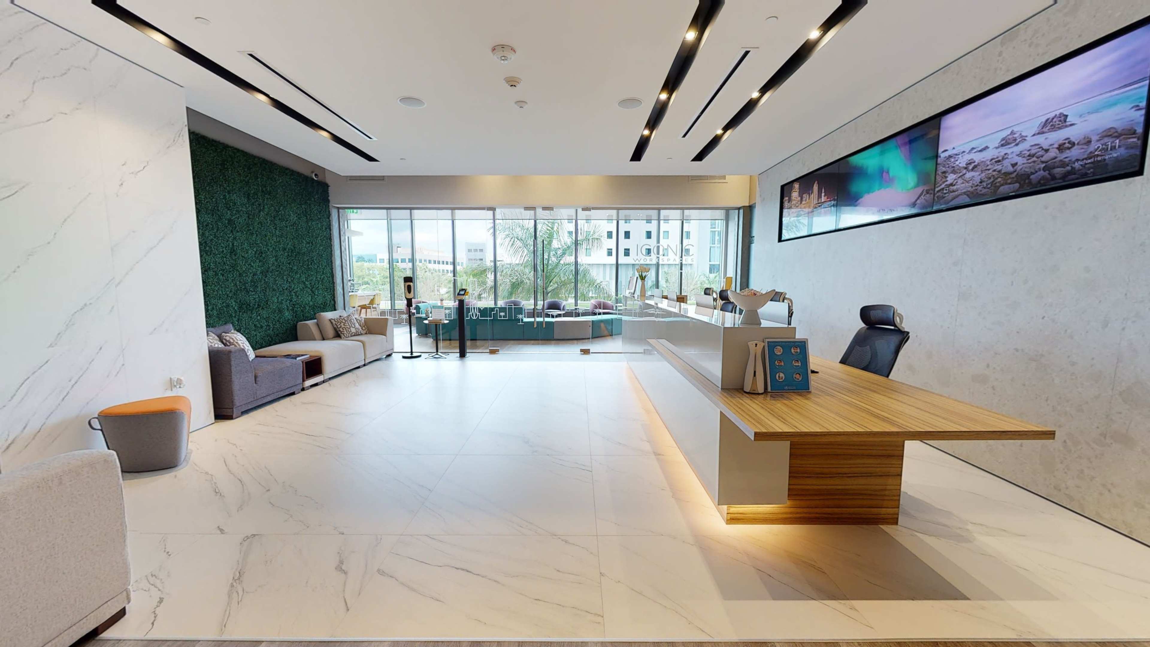 A spacious lobby featuring a reception desk, seating areas, large windows with a view, and decorative wall elements.