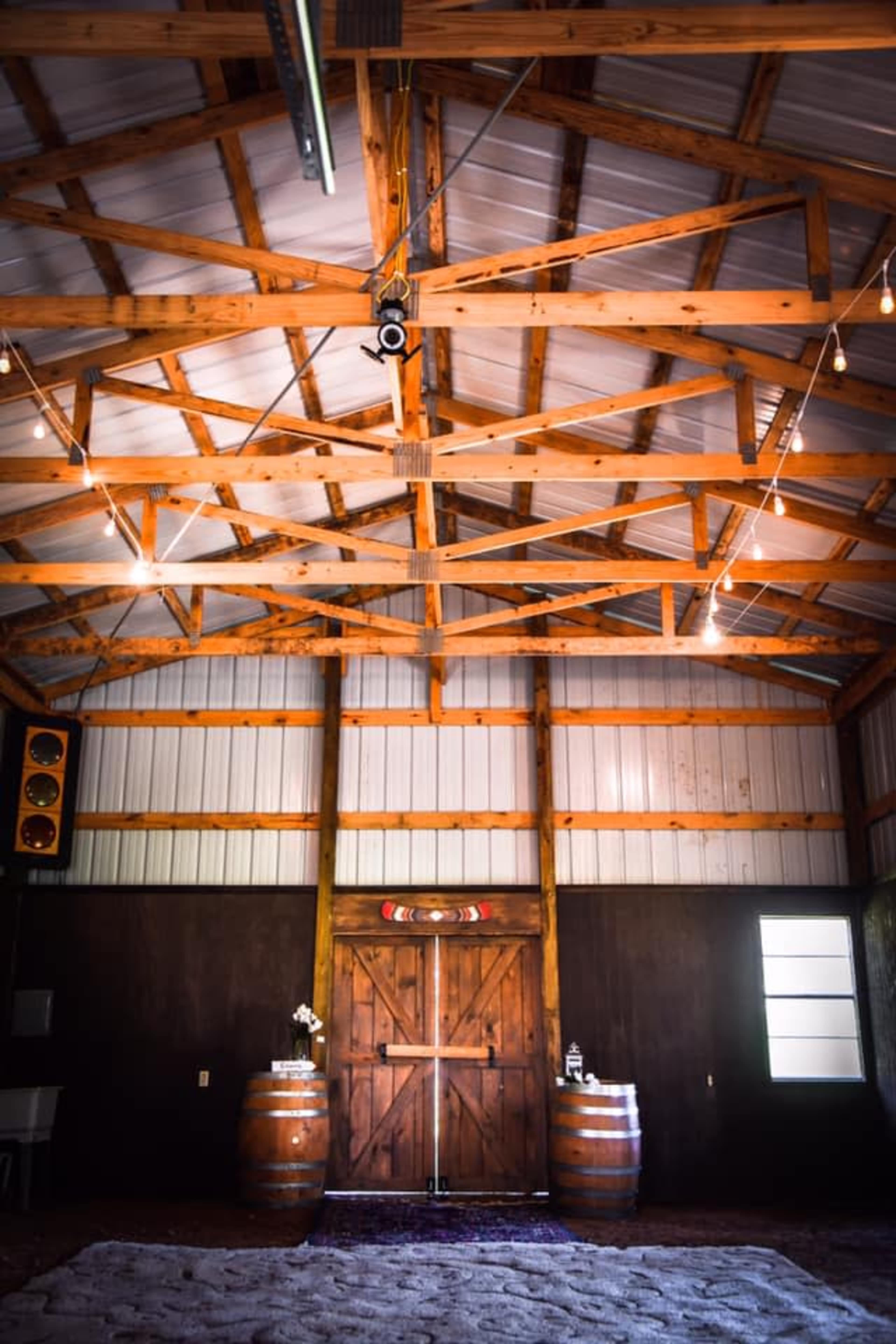 The image shows the interior of a barn with wooden beams, two barrels near the entrance, and a large double door at the back.