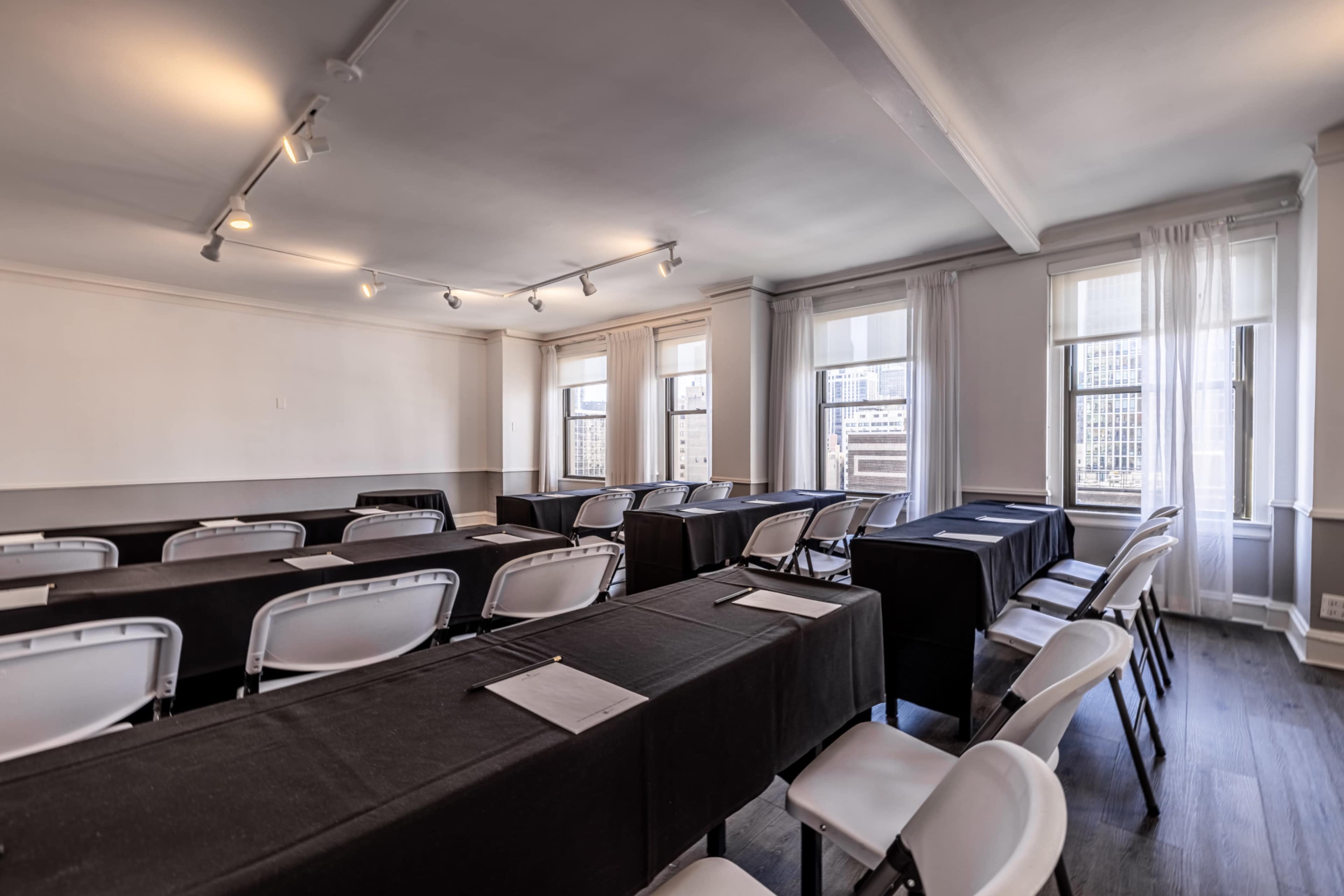 The image shows a conference room set up with several tables covered in black tablecloths and white chairs arranged in a row.