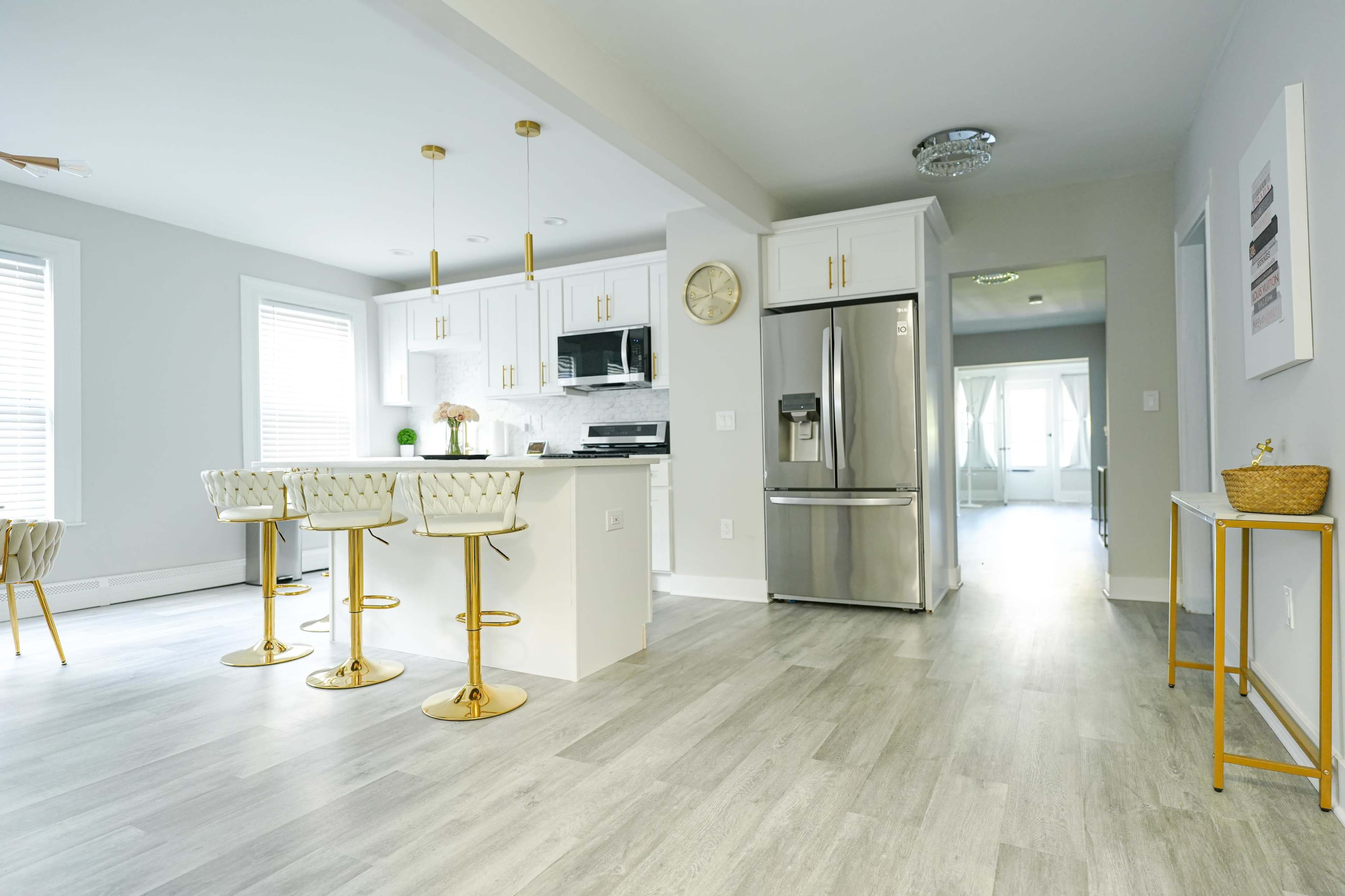 A modern kitchen with white cabinetry, stainless steel appliances, and gold-accented bar stools around a central island.