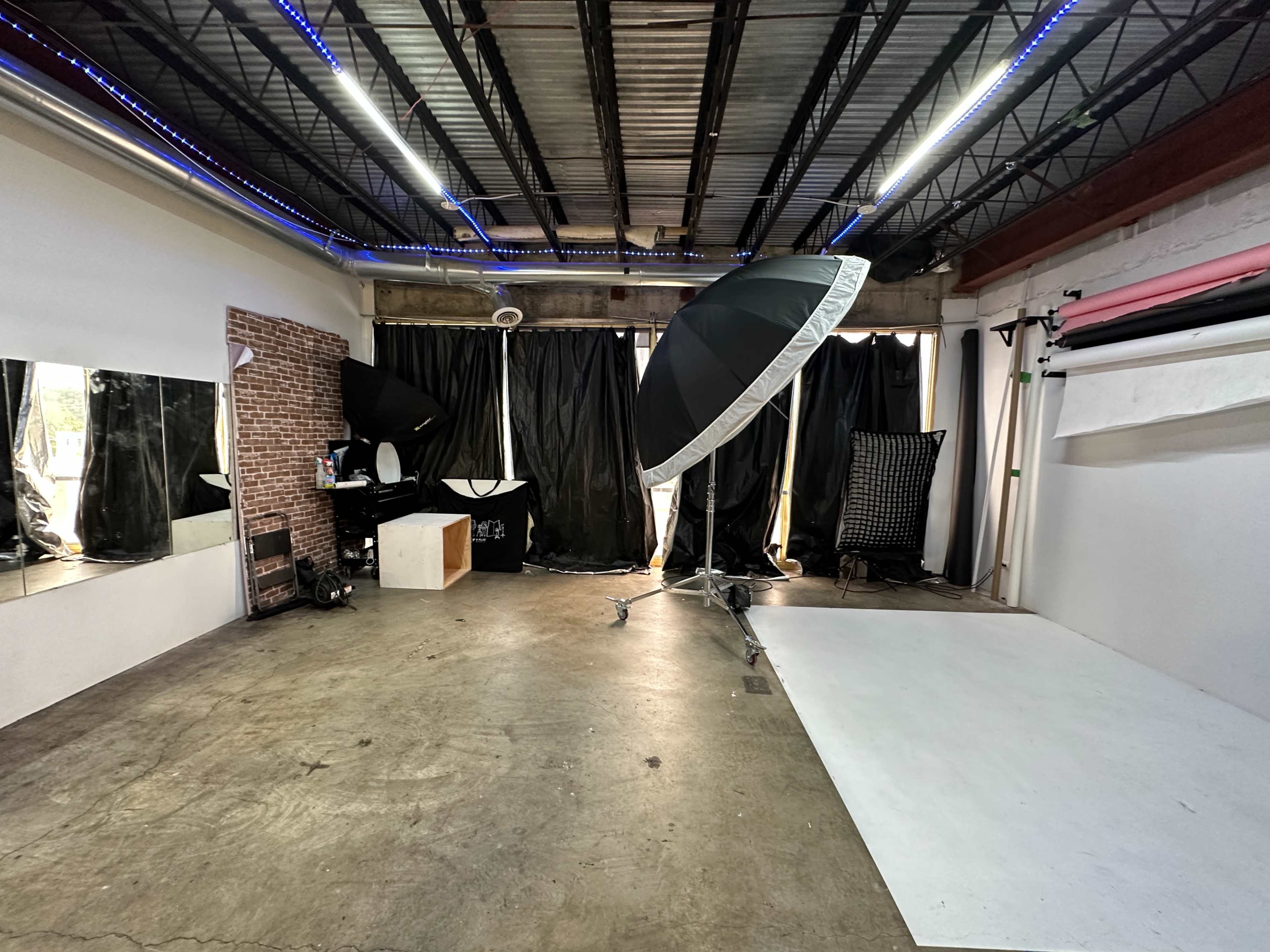 A photography studio with a large softbox light, black curtains, a white backdrop, and various equipment arranged around the space.