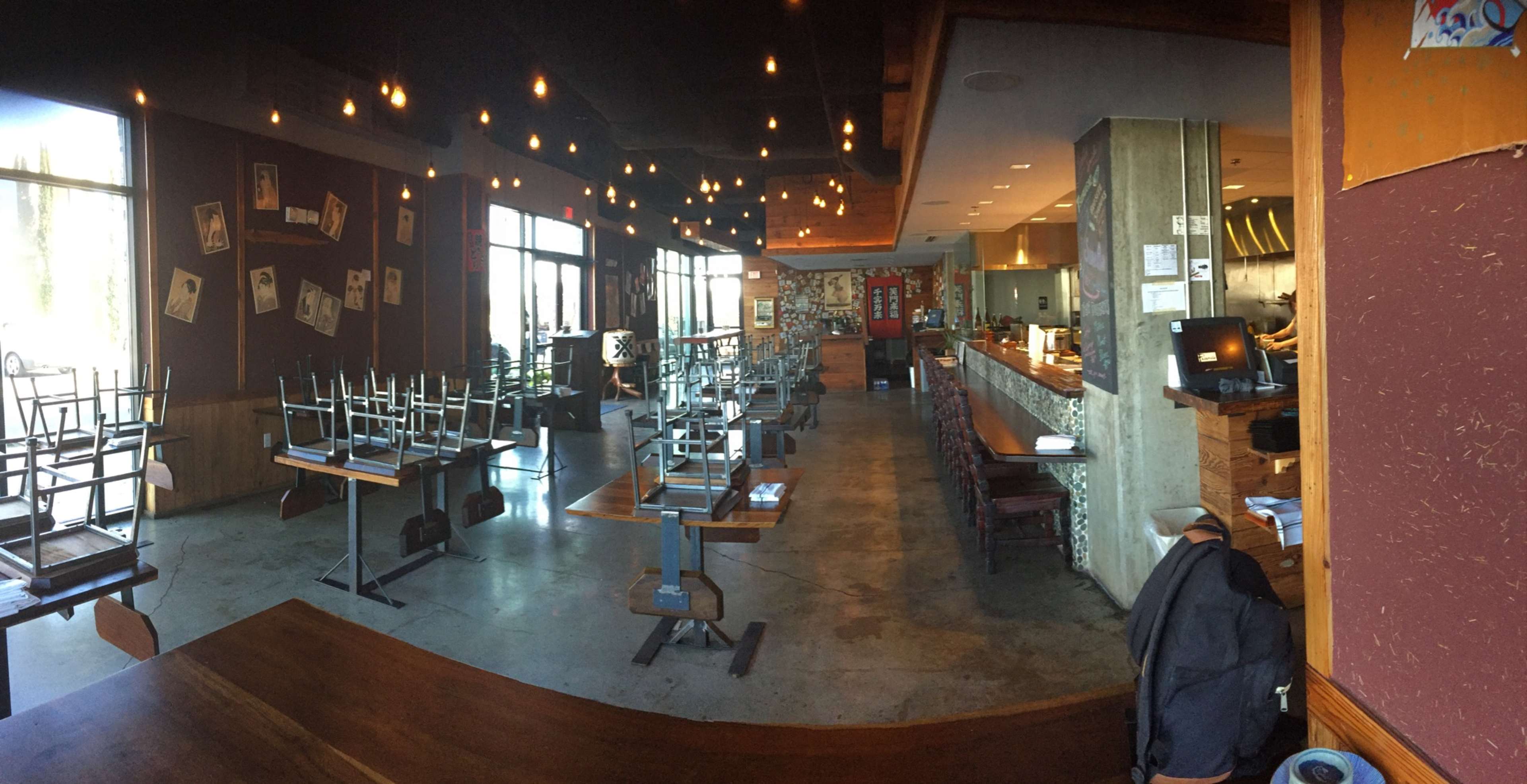 The image shows a partially empty restaurant with overturned chairs stacked on tables, exposed light bulbs hanging from the ceiling, and a visible kitchen area at the back.