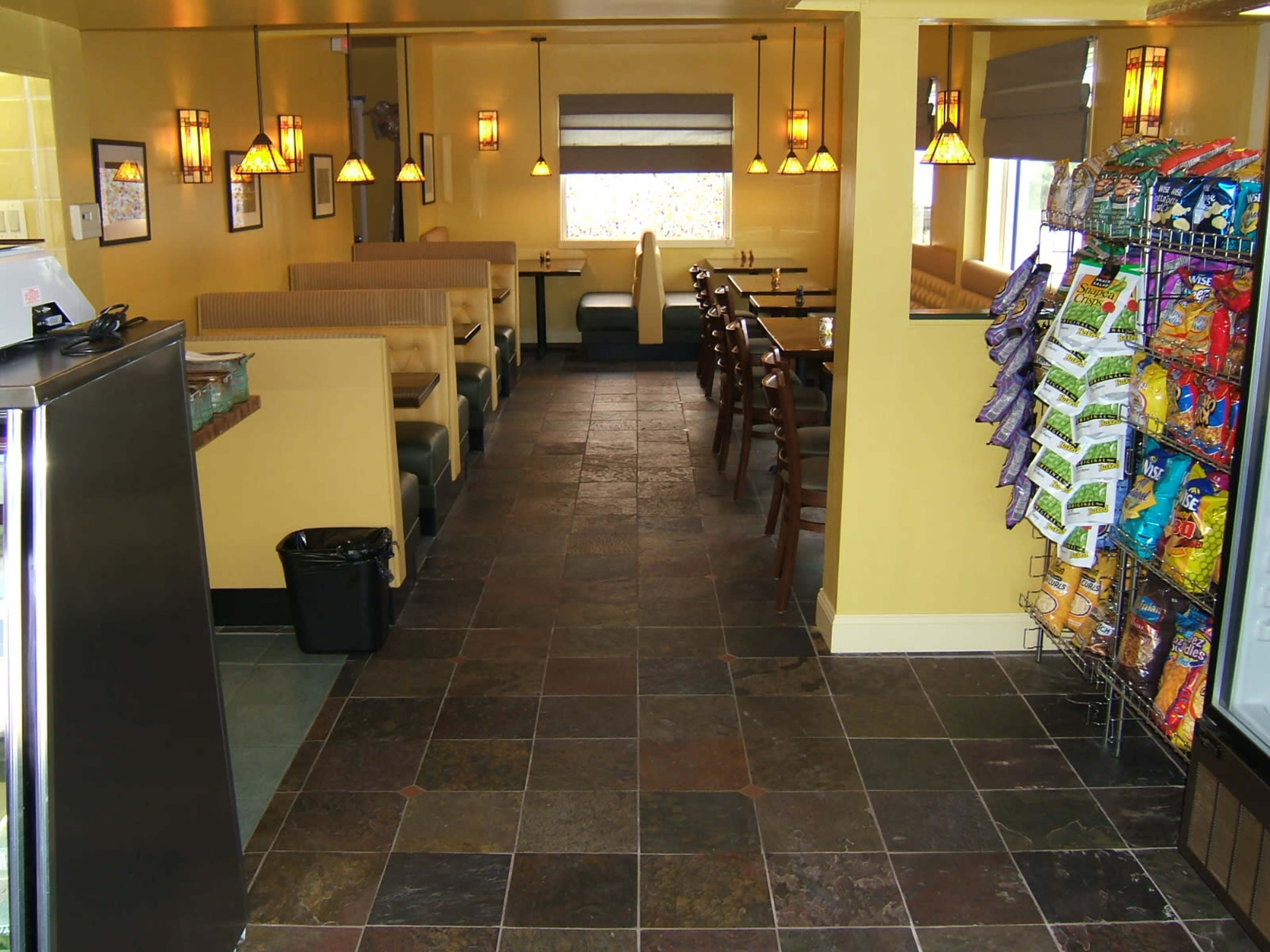 A restaurant interior with seating booths along the walls, tables in the center, and a display rack of snacks on one side.