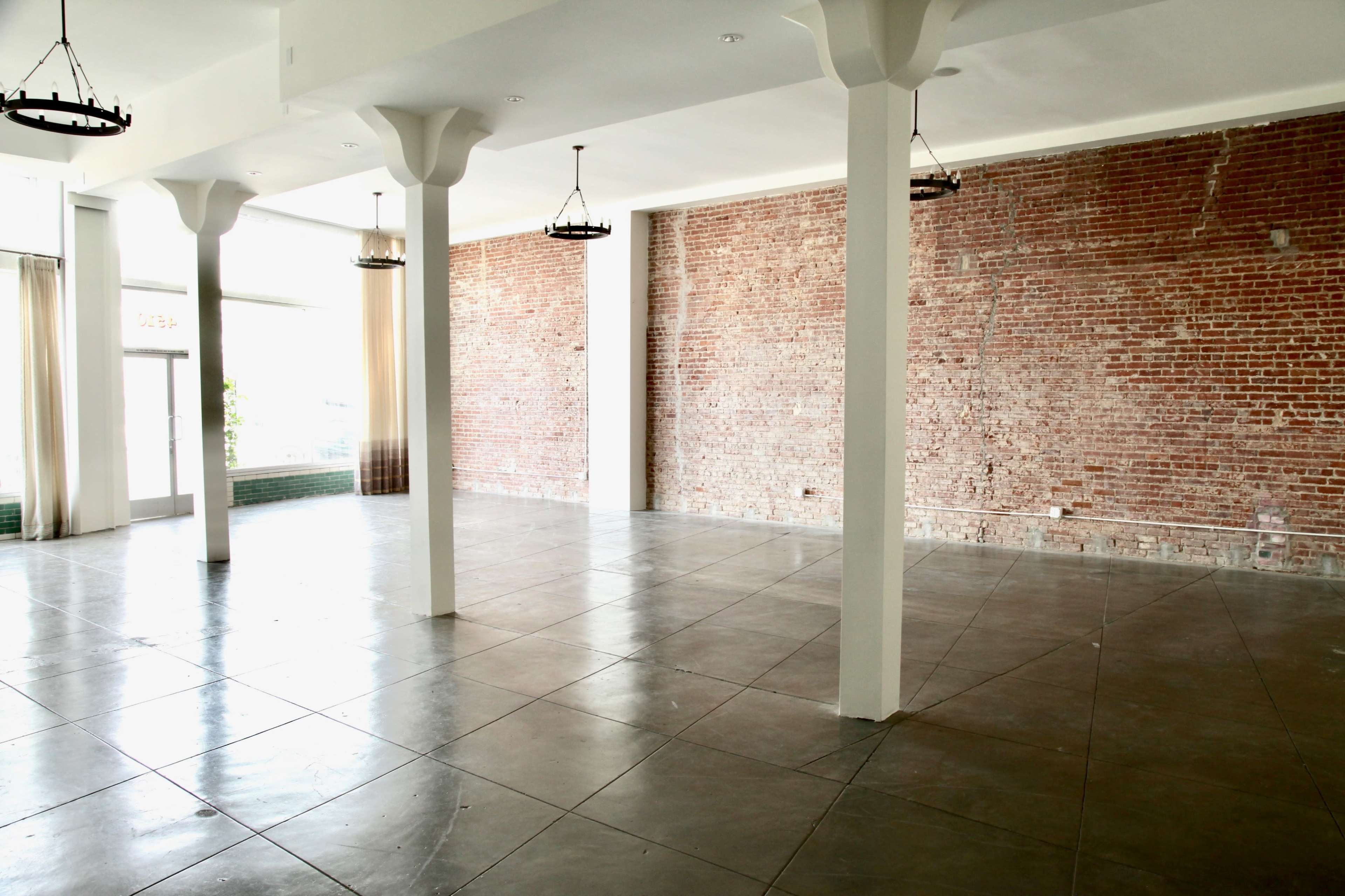 An empty room with polished concrete floors, exposed brick walls, and several pendant lights hanging from the ceiling.
