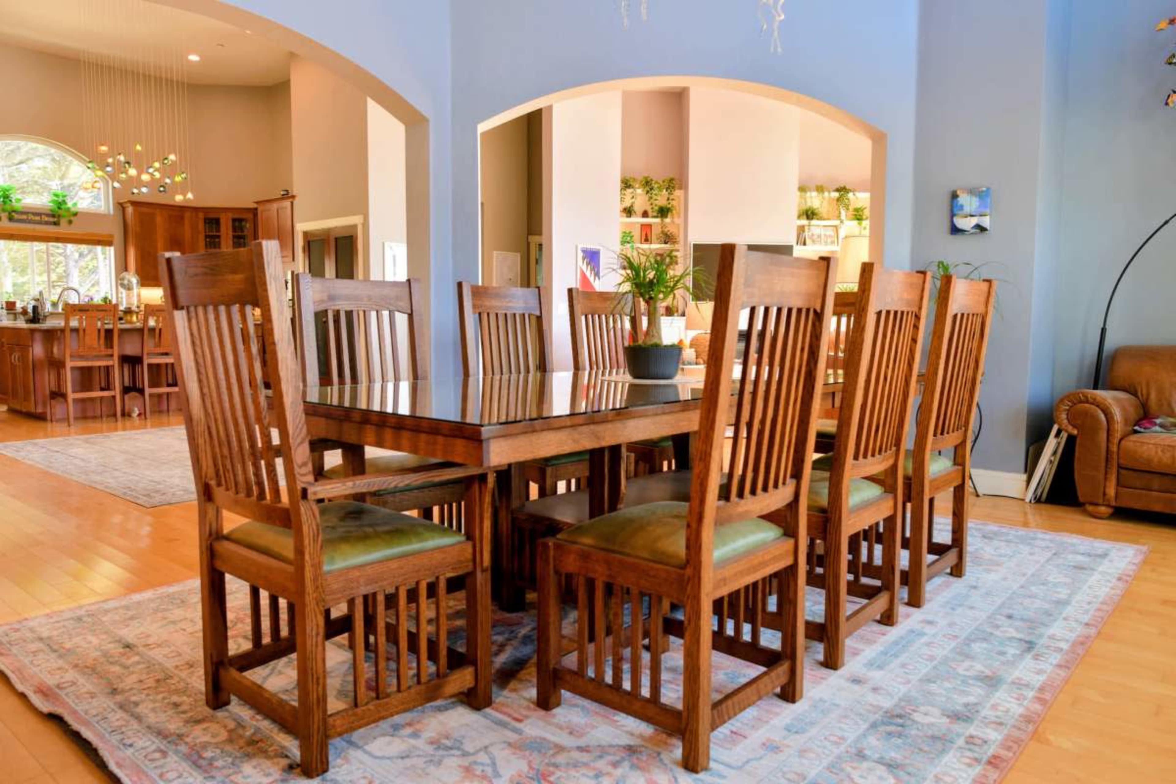 A large wooden dining table with twelve chairs is set in a spacious room featuring arched doorways and a visible kitchen area in the background.