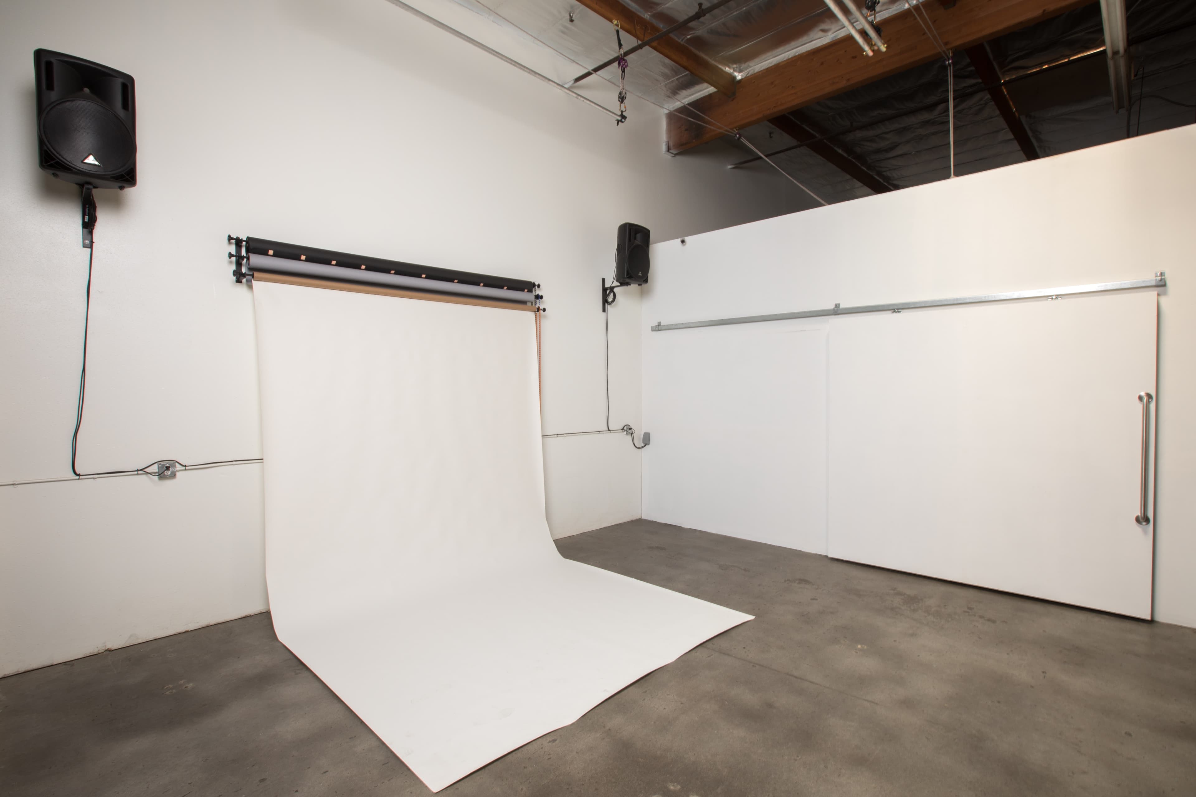 A photography studio with a white backdrop, concrete floor, and ceiling-mounted lighting.