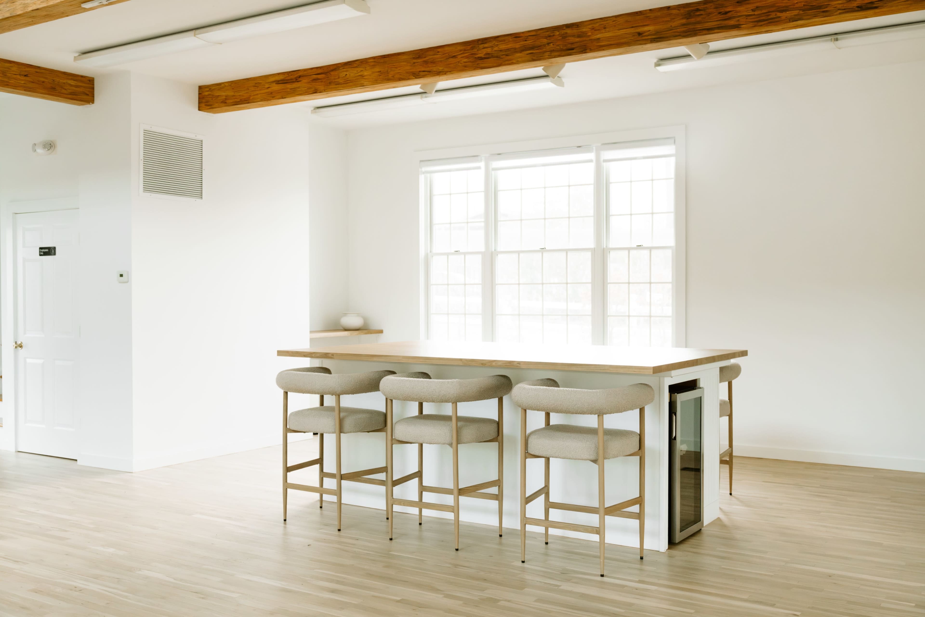 A modern kitchen features a wooden countertop with four cushioned bar stools, positioned in front of large windows.