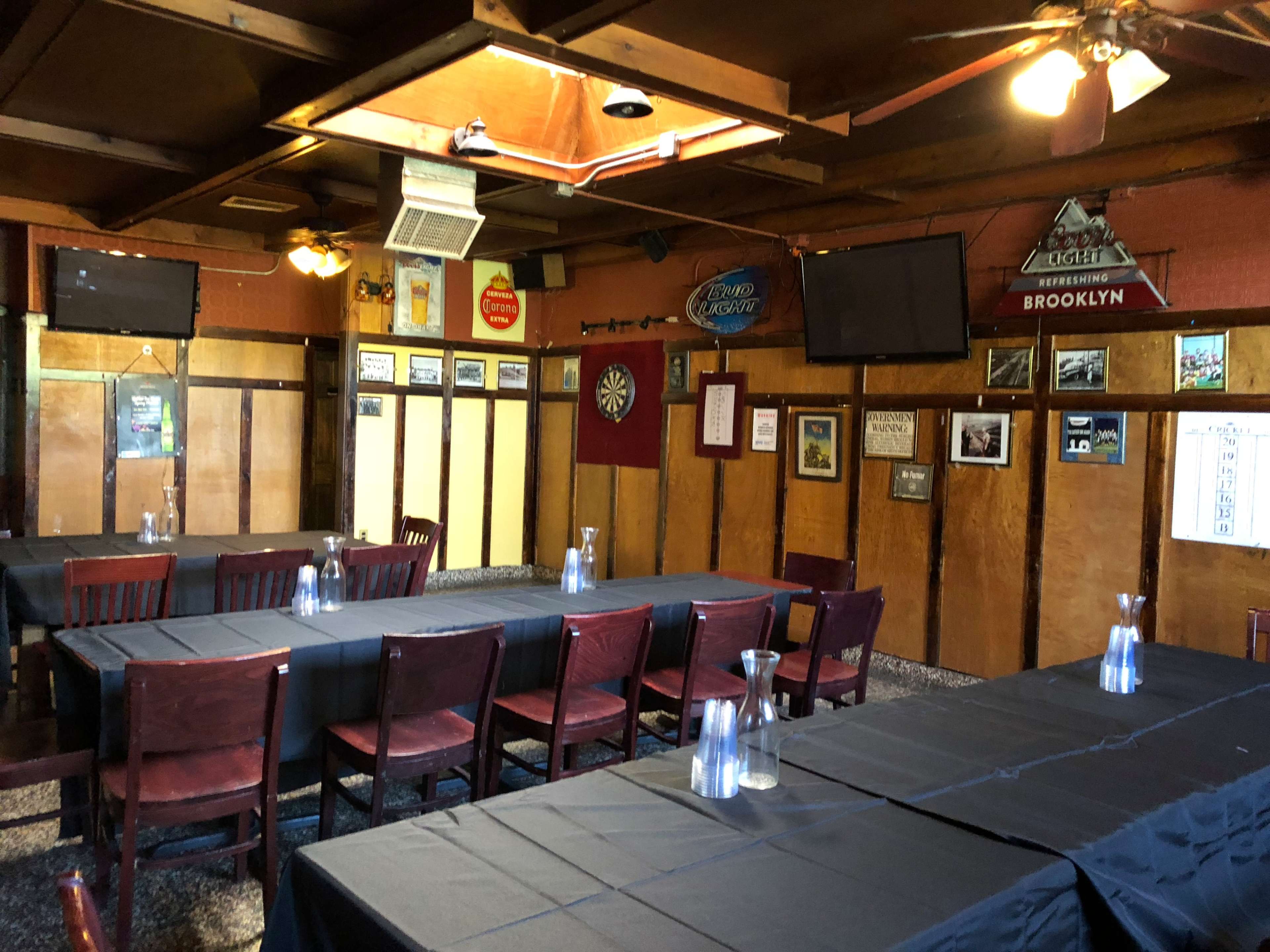 A rustic dining room features several tables covered with black tablecloths, wooden chairs, and walls adorned with various signs and framed pictures.