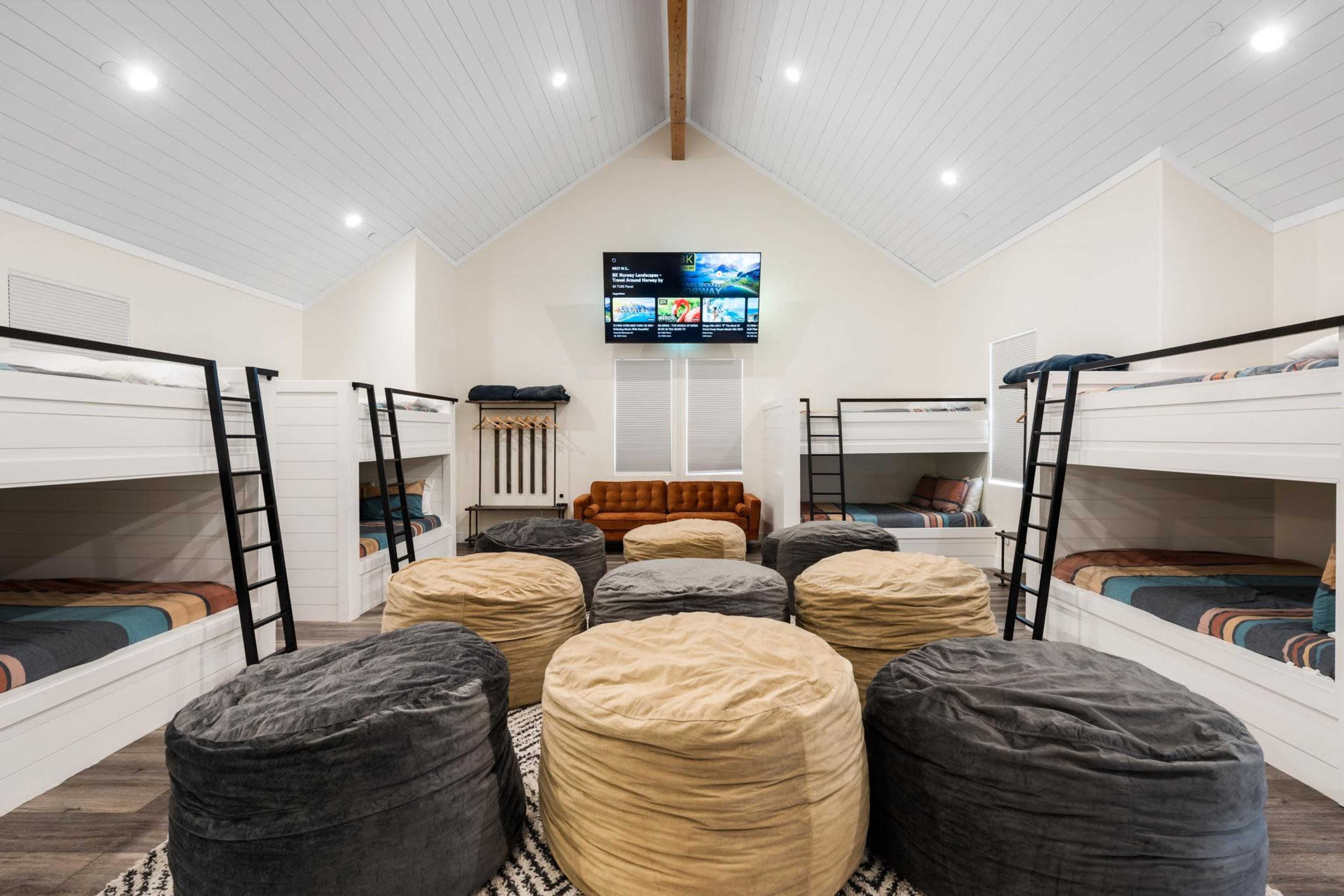 A modern bunk room with two sets of bunk beds, multiple bean bags, and a television mounted on the wall.