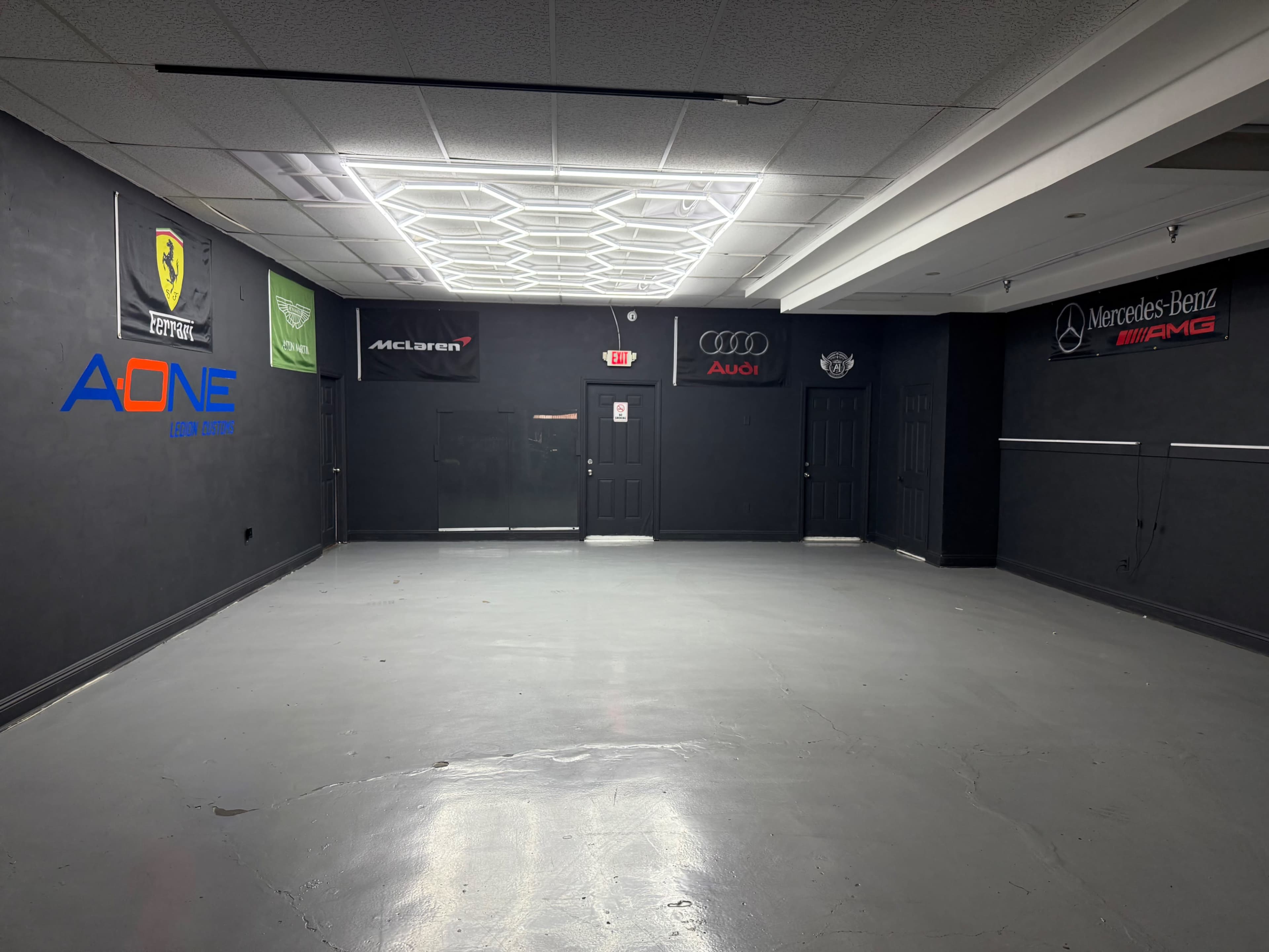 The image shows a spacious, empty room with black walls adorned with various car brand logos, including Ferrari, McLaren, Audi, and Mercedes-Benz.