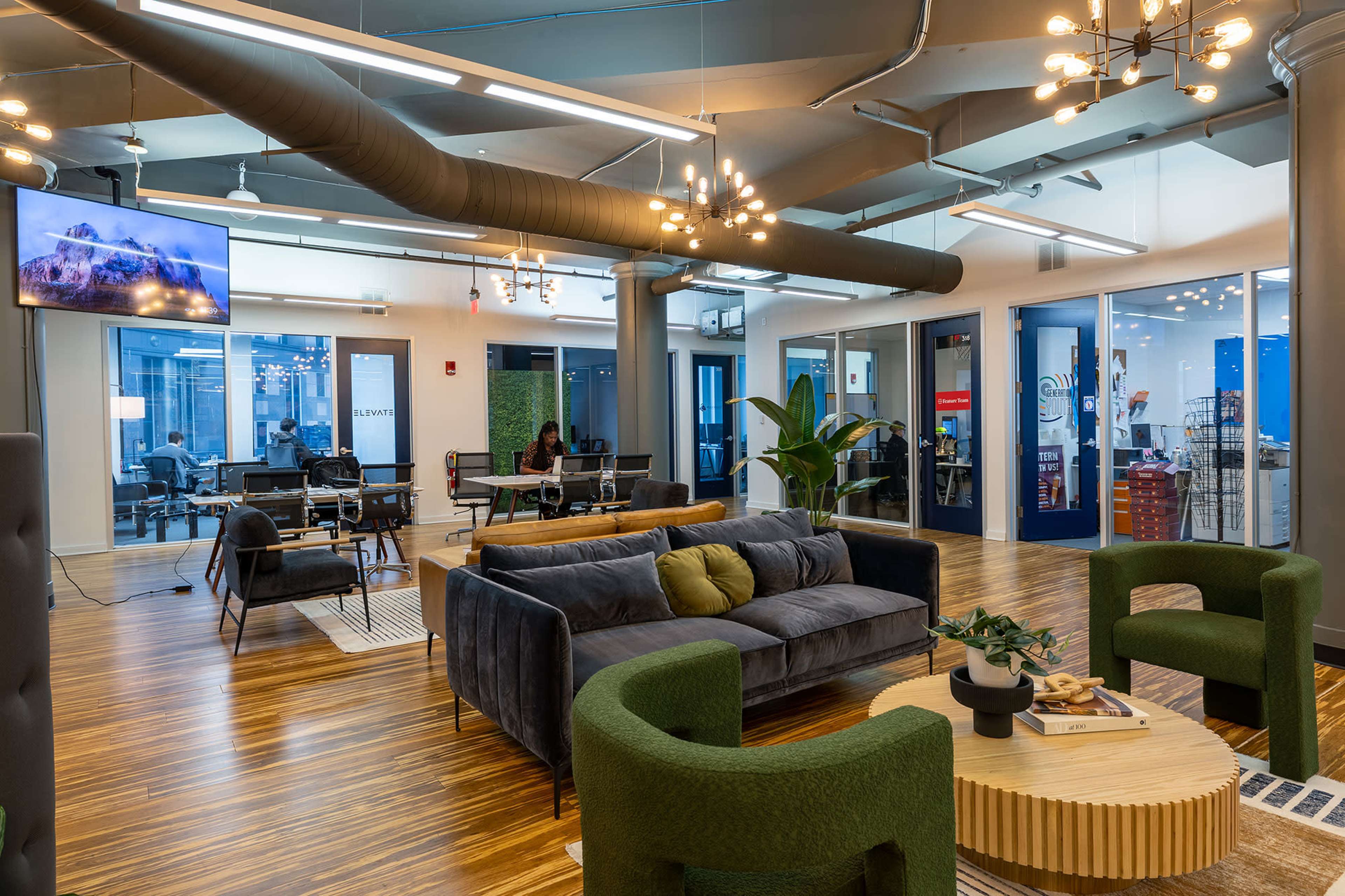 The image shows a modern office space with a lounge area featuring green chairs, a gray sofa, a coffee table, and workstations visible in the background.