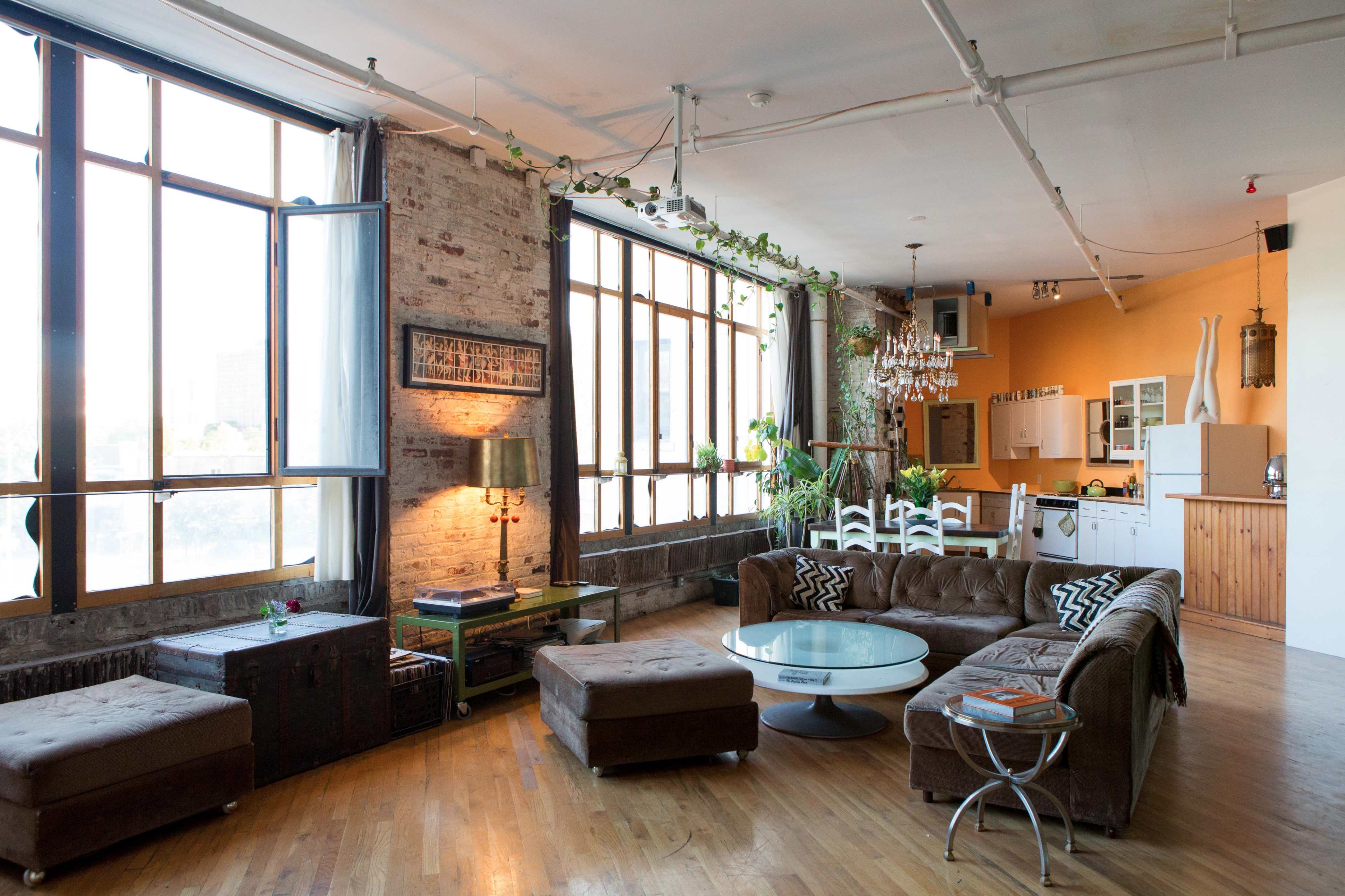 A spacious, modern loft with large windows, a comfortable seating area, and an open kitchen in the background.