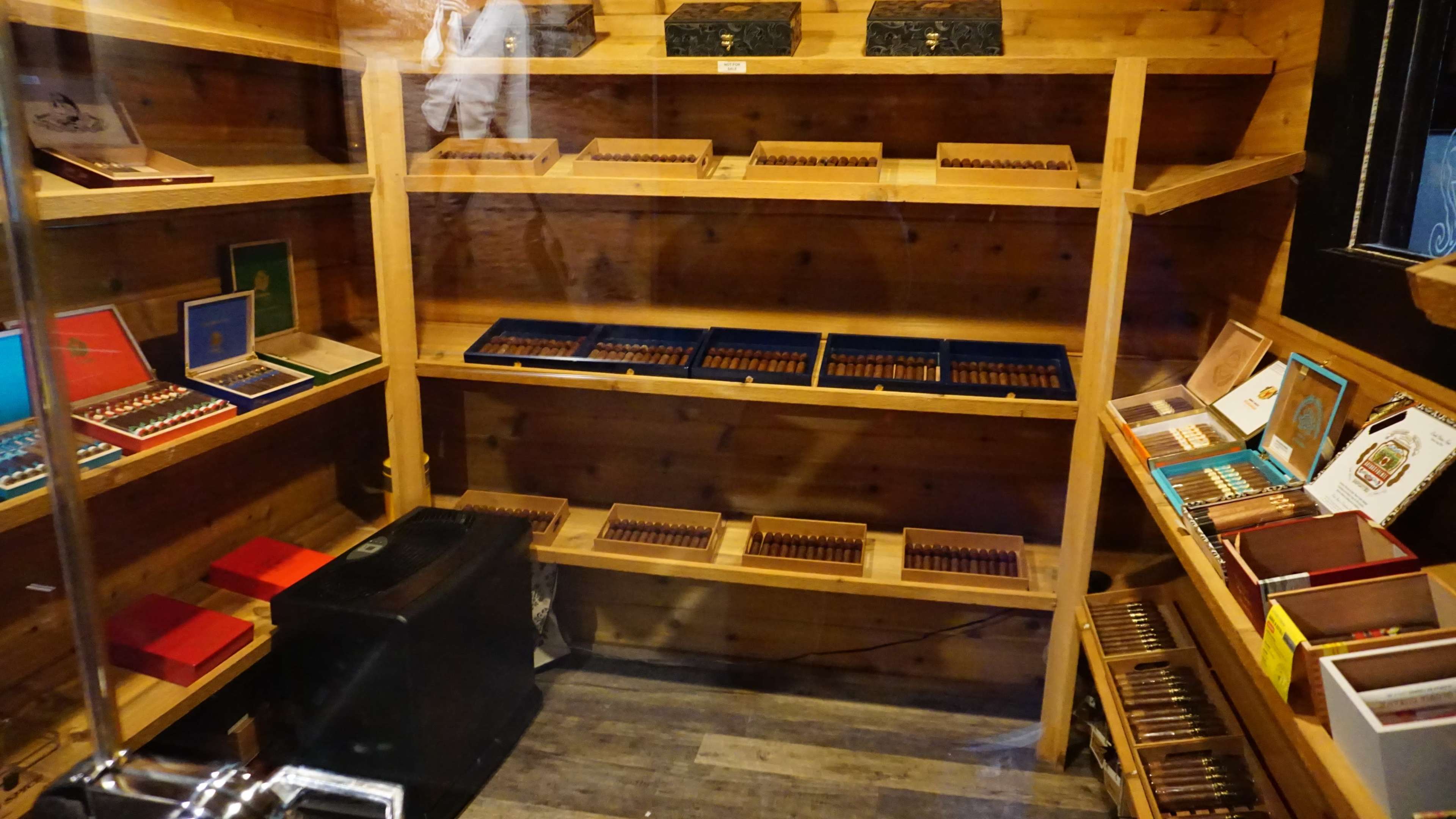 The image shows a wooden display case with several shelves filled with arranged boxes of cigars.