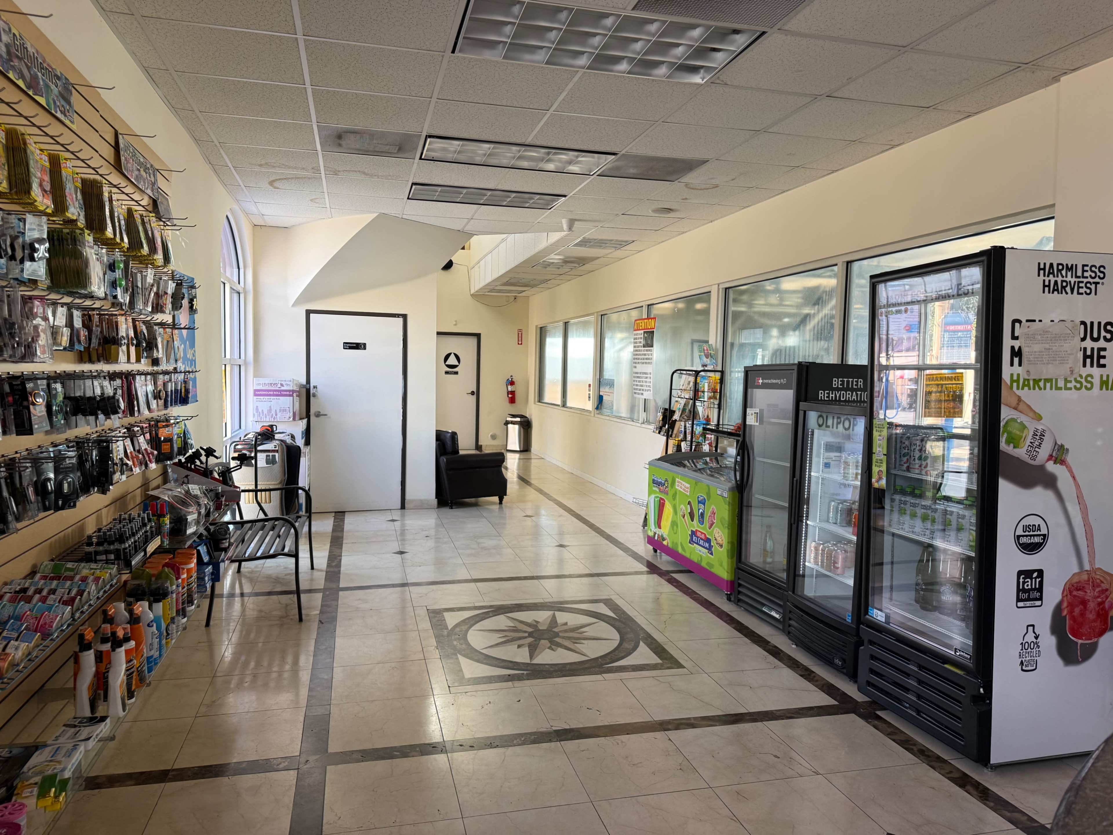The image shows a spacious interior of a store with shelves stocked on the left, a drink cooler on the right, and a reception area ahead.