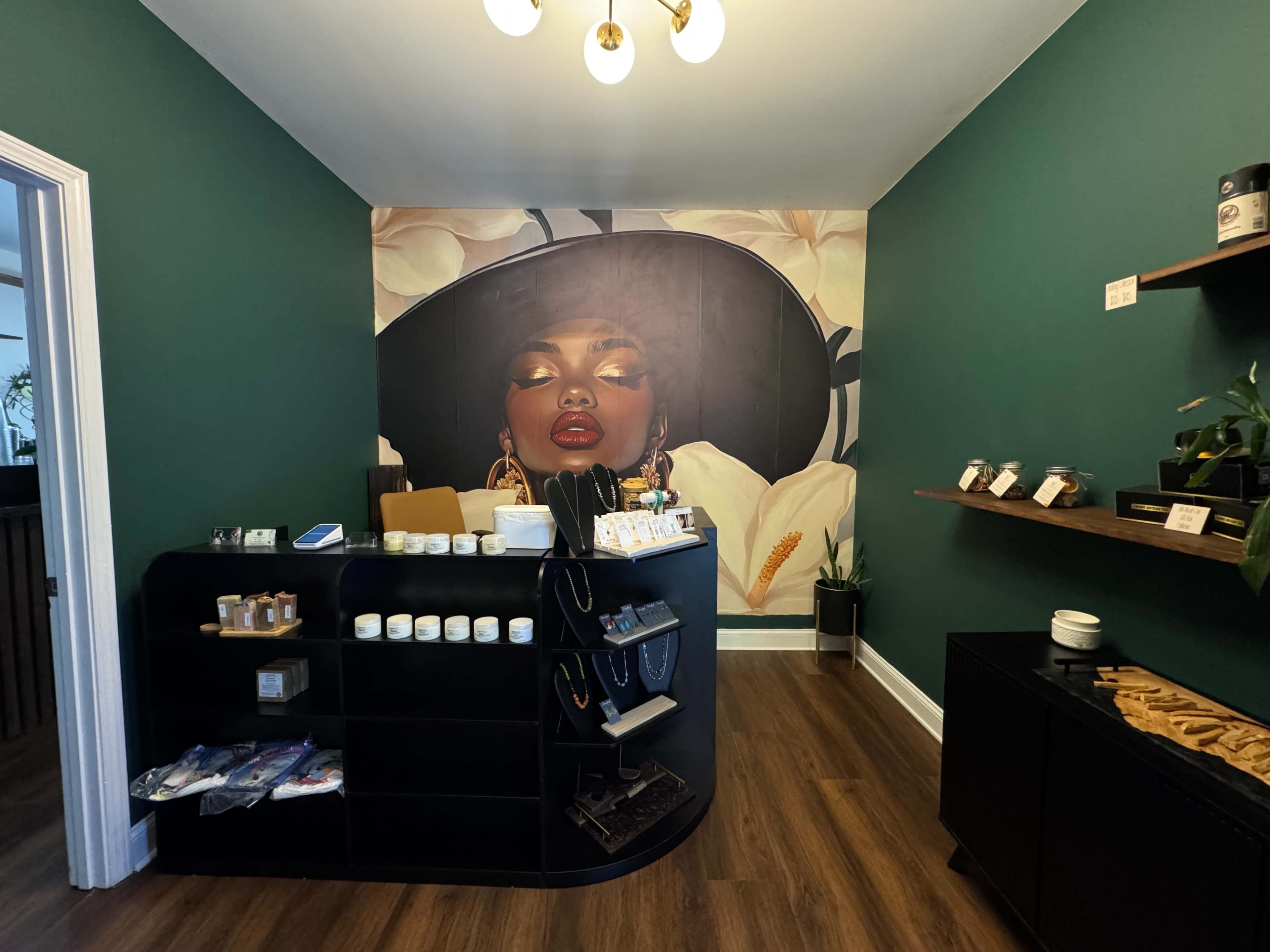 The image shows a boutique interior with a dark green wall featuring a large mural of a woman's face, along with a stylish display counter and shelves holding various products.
