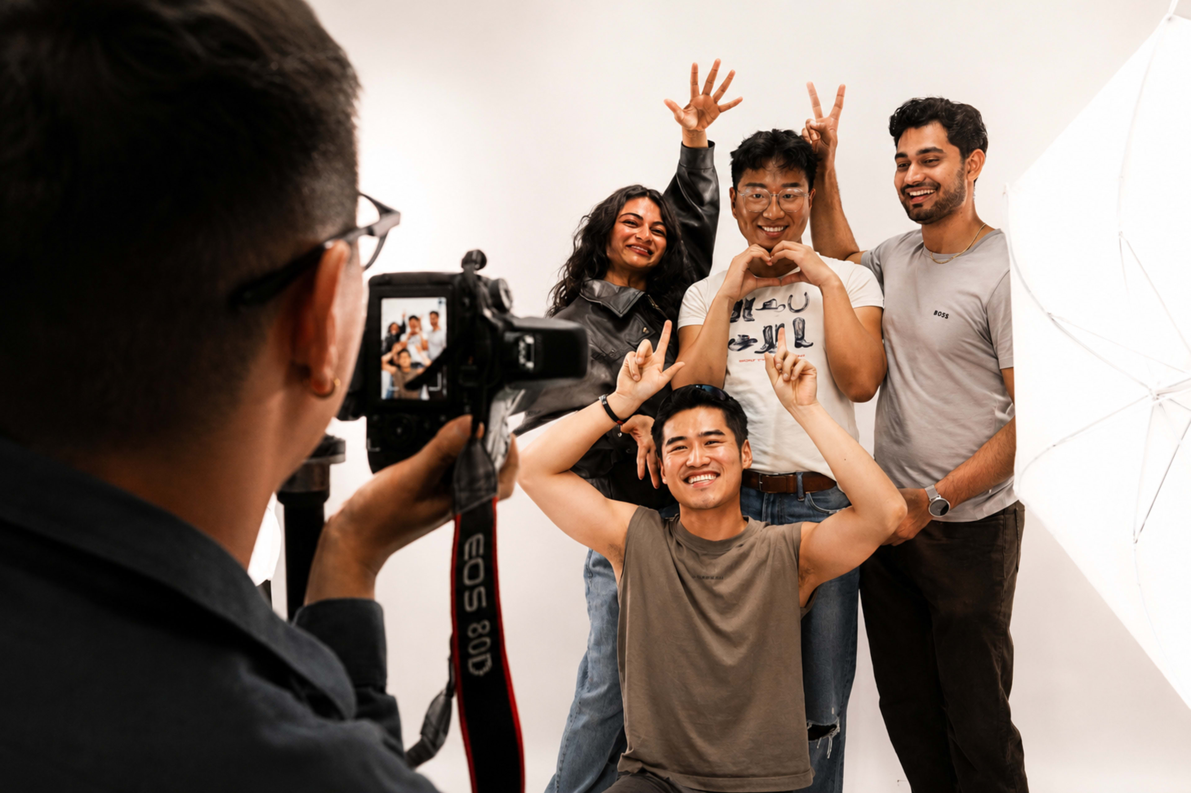 A group of four people pose for a photo in front of a camera, with one person taking the picture and the others making playful gestures.
