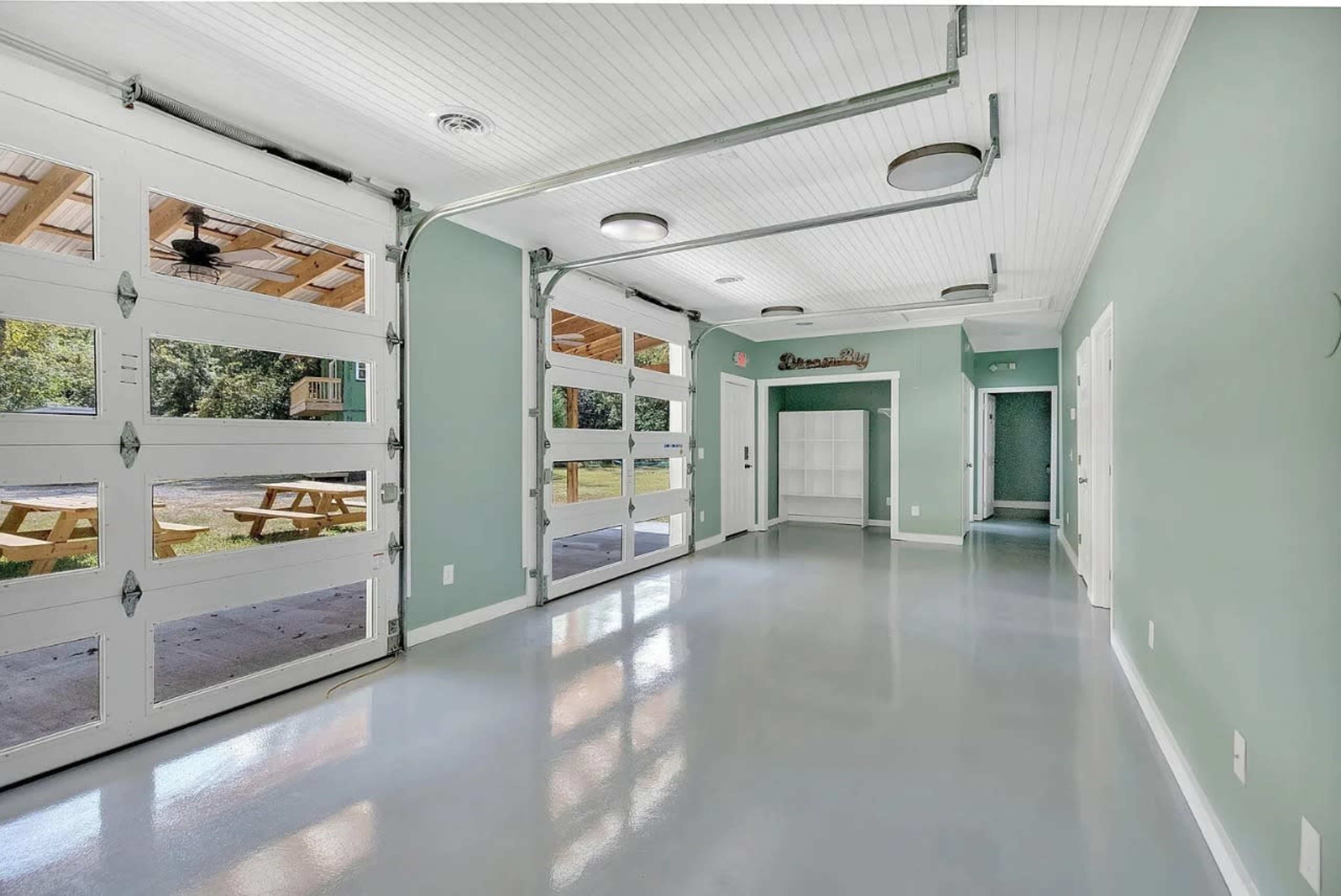 The image shows a spacious, well-lit garage or utility room with large glass doors, a smooth floor, and pale green walls.