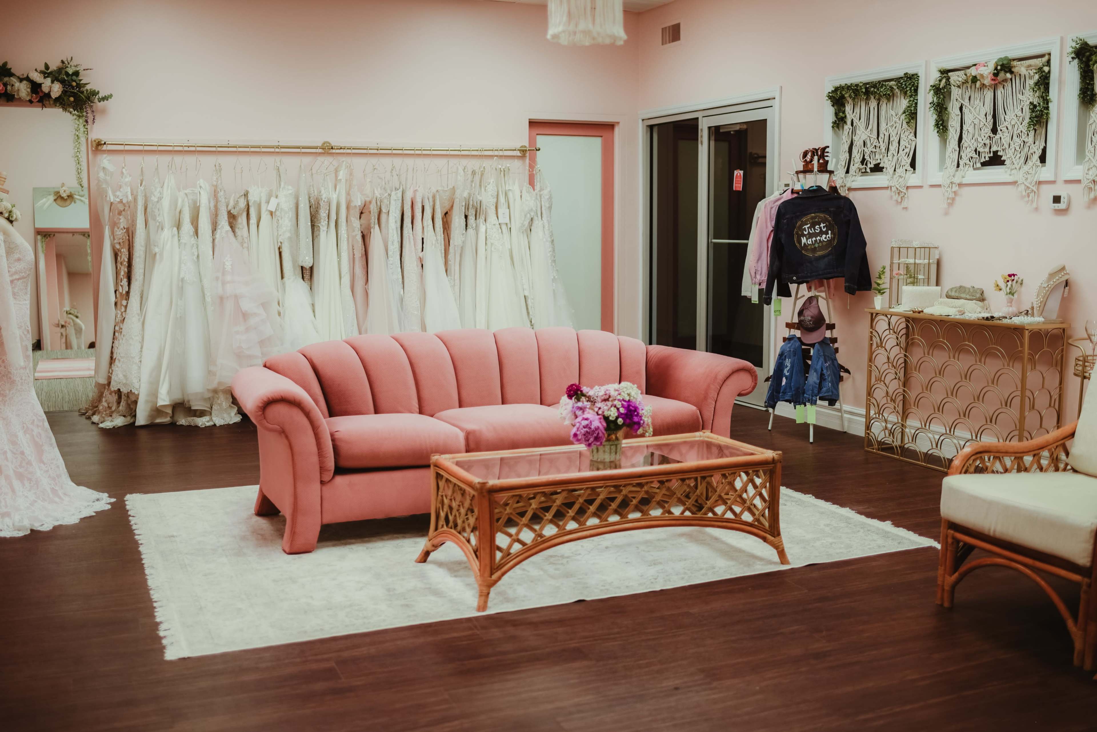 A pink boutique interior with a pink couch, a coffee table, and a rack of wedding dresses in the background.